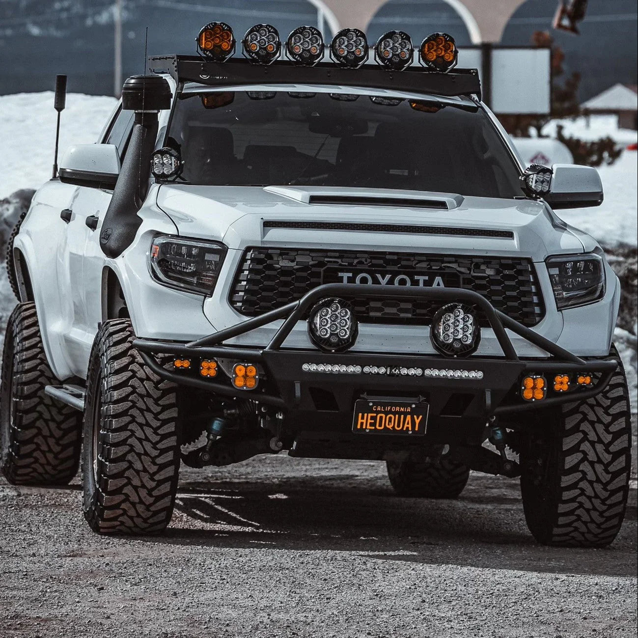 White Toyota Tundra with off-road upgrades, LED lights, roof rack and rugged tires in a snowy setting