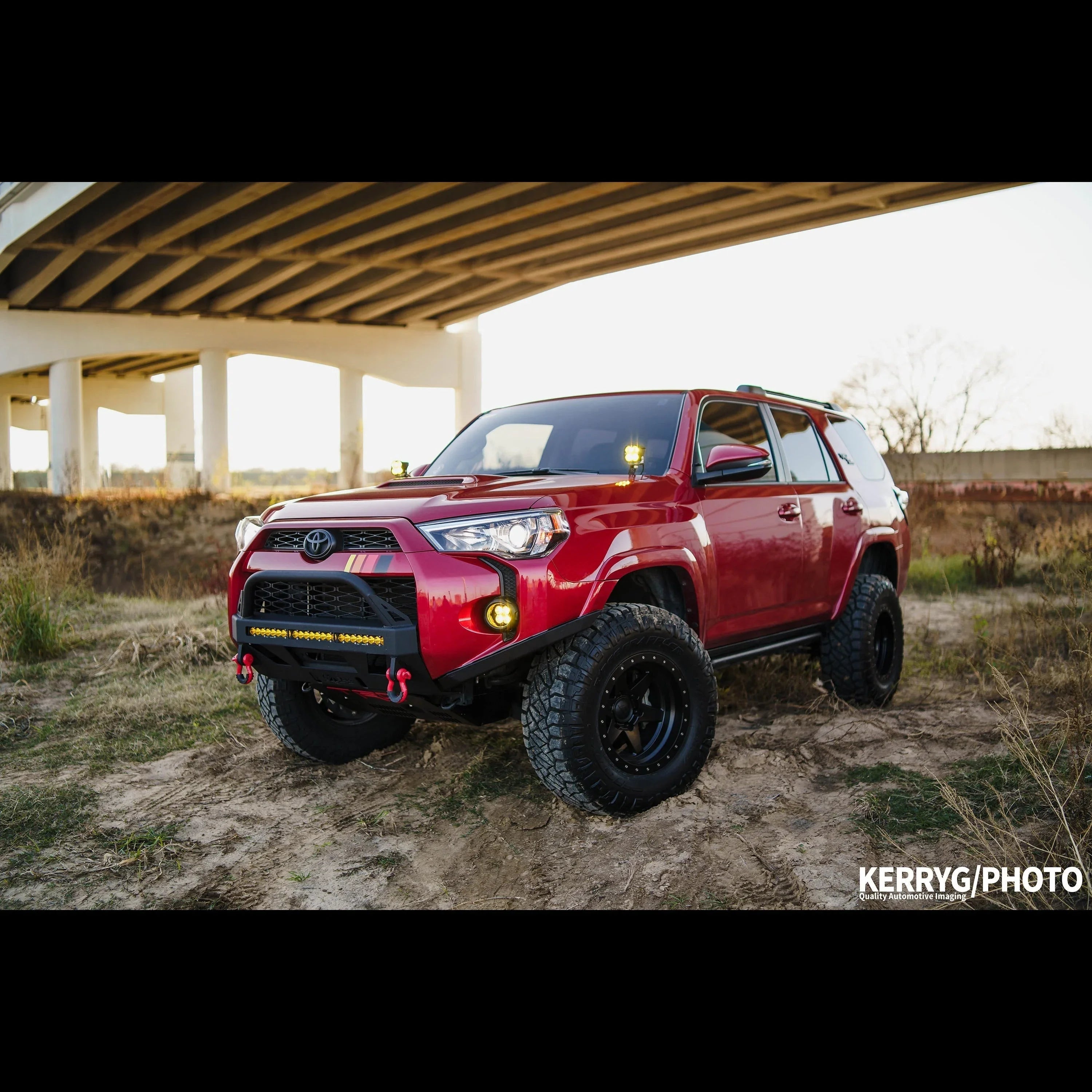 Lifted red Toyota 4Runner with off-road accessories parked under a bridge outdoors