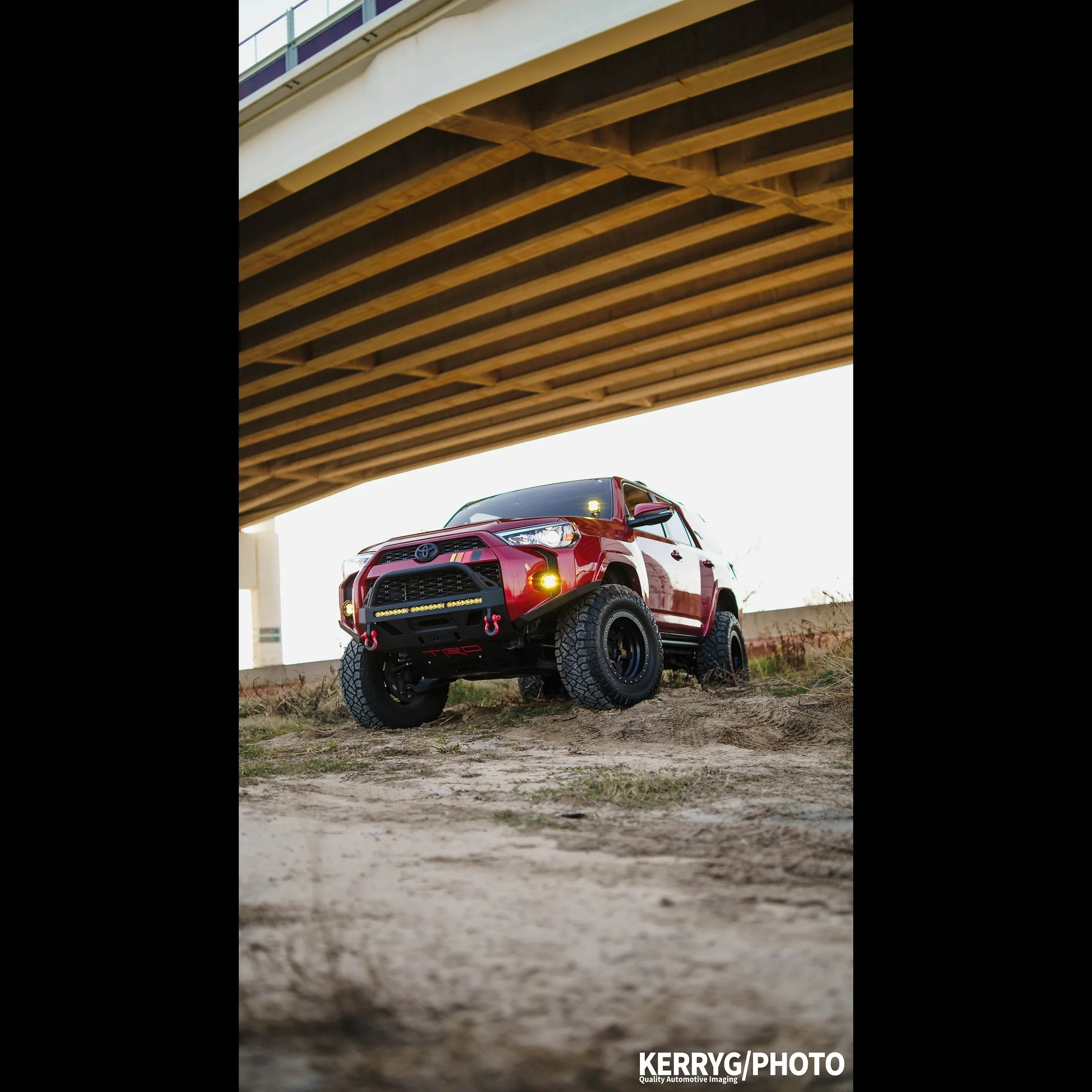 Red Toyota 4Runner with off-road modifications parked outdoors under a bridge