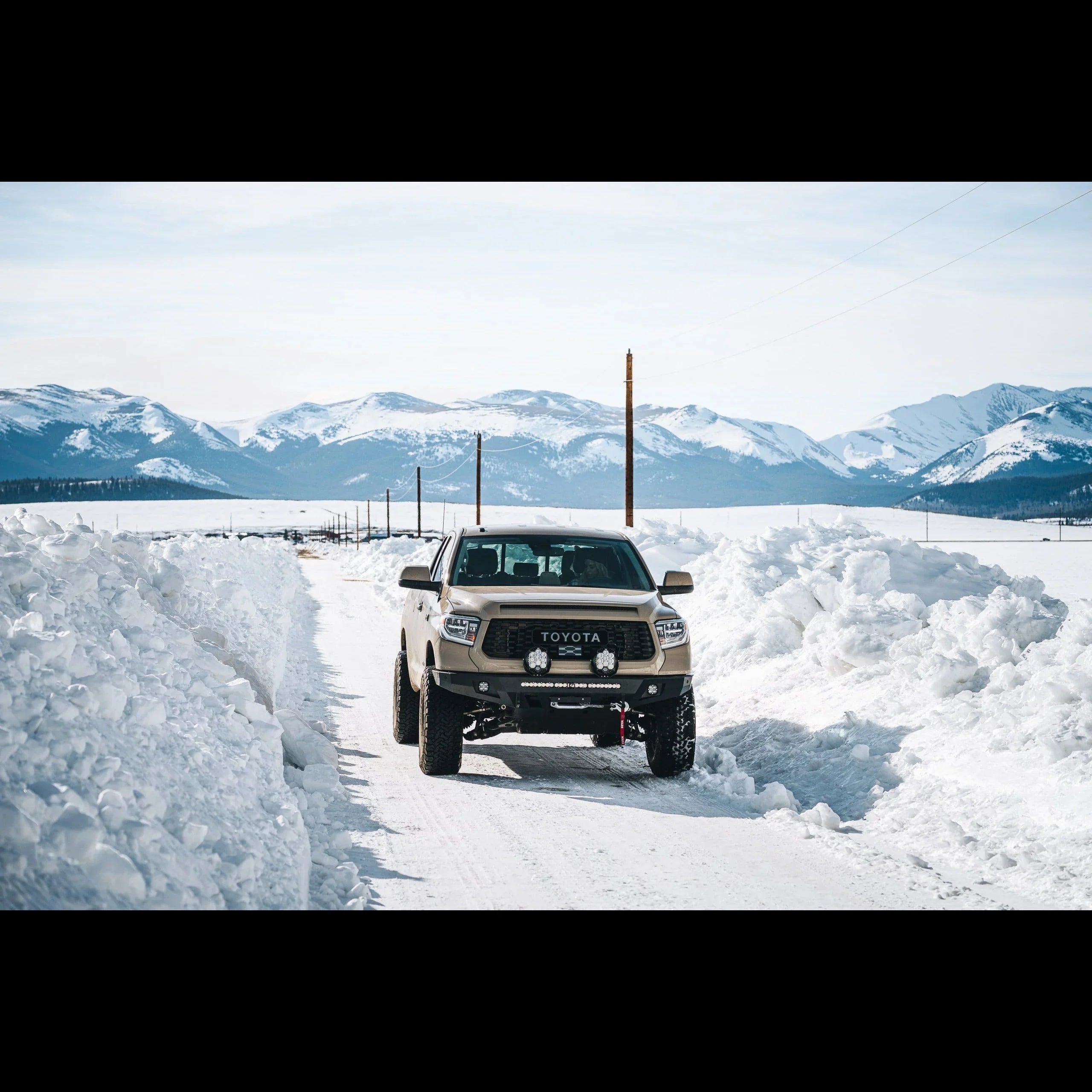 Toyota Tacoma off-road truck driving on snowy trail with mountains in background