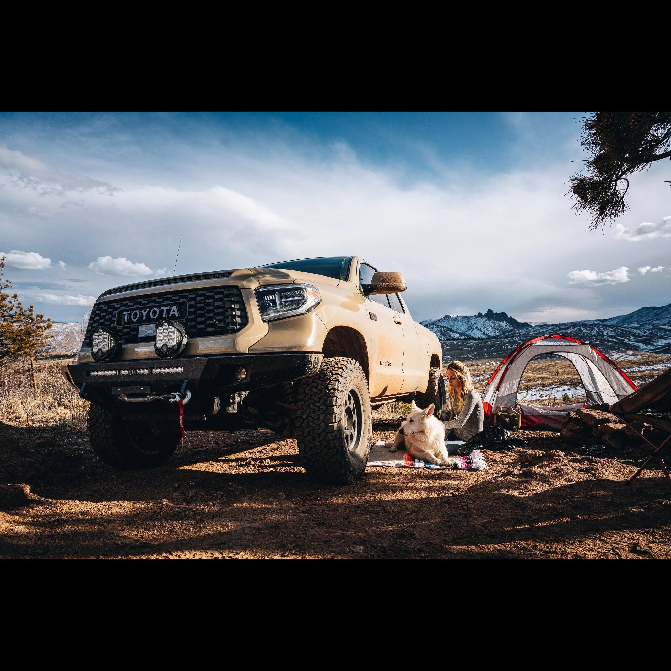 Toyota Tundra off-road truck, camping gear, woman and dog outdoors in a mountain landscape