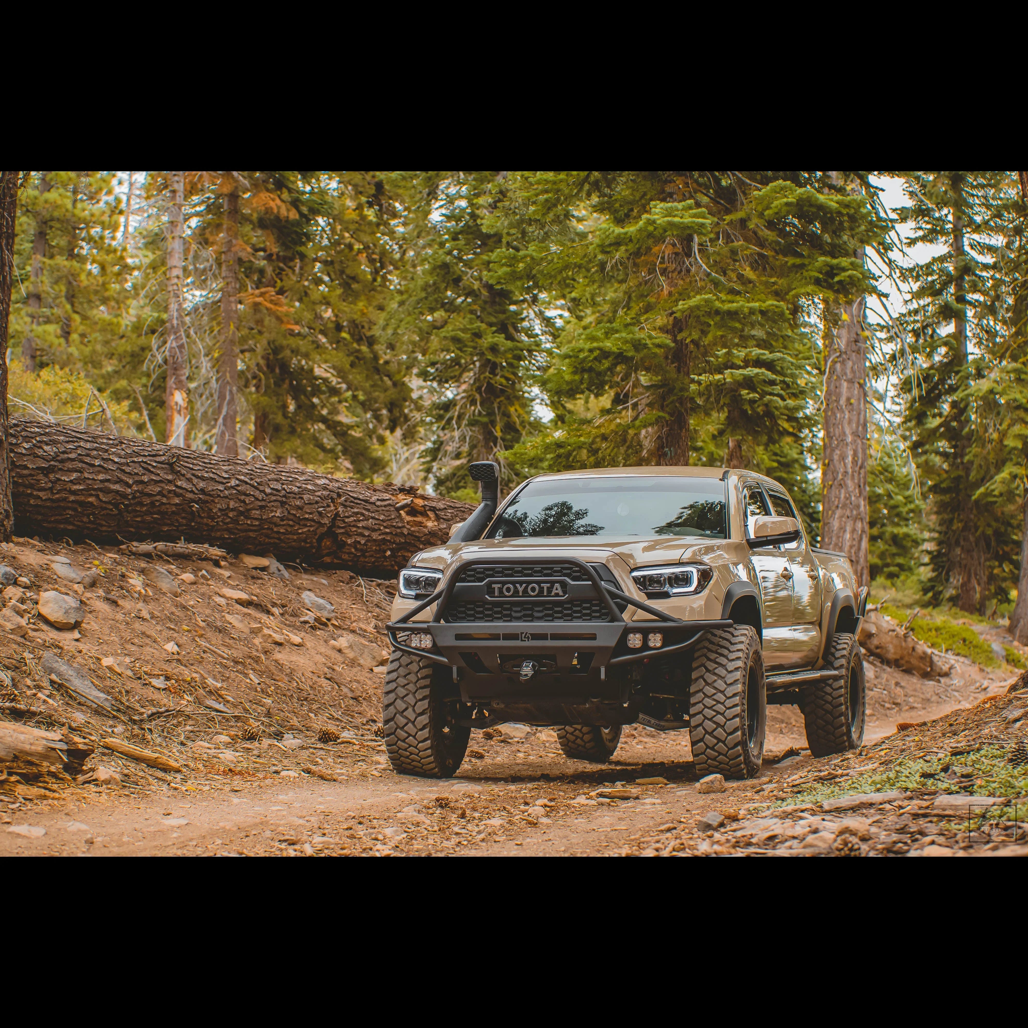 Lifted Toyota Tacoma off-road truck with large tires and snorkel on a rocky forest trail
