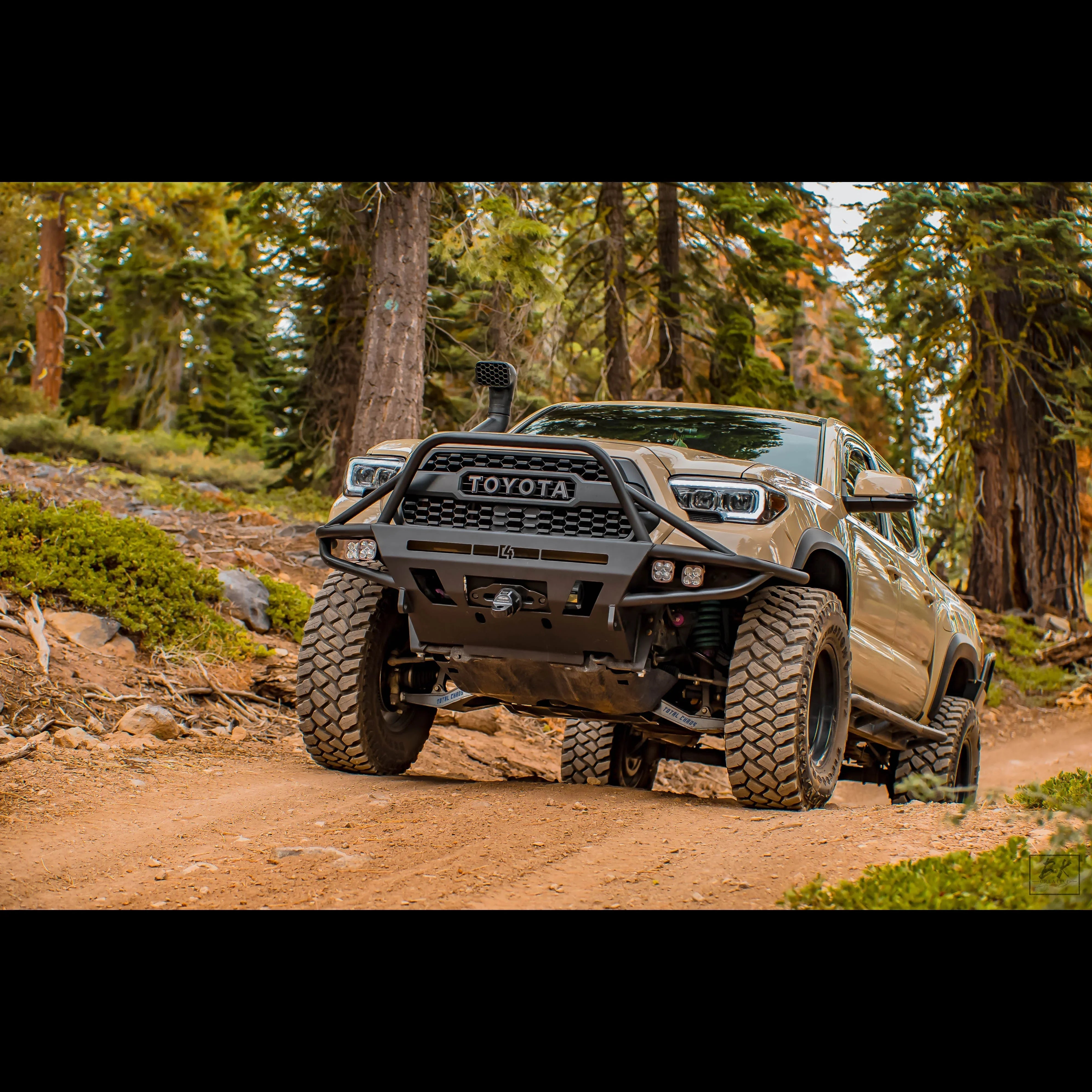 Toyota Tacoma overland truck with off-road accessories on a forest dirt trail