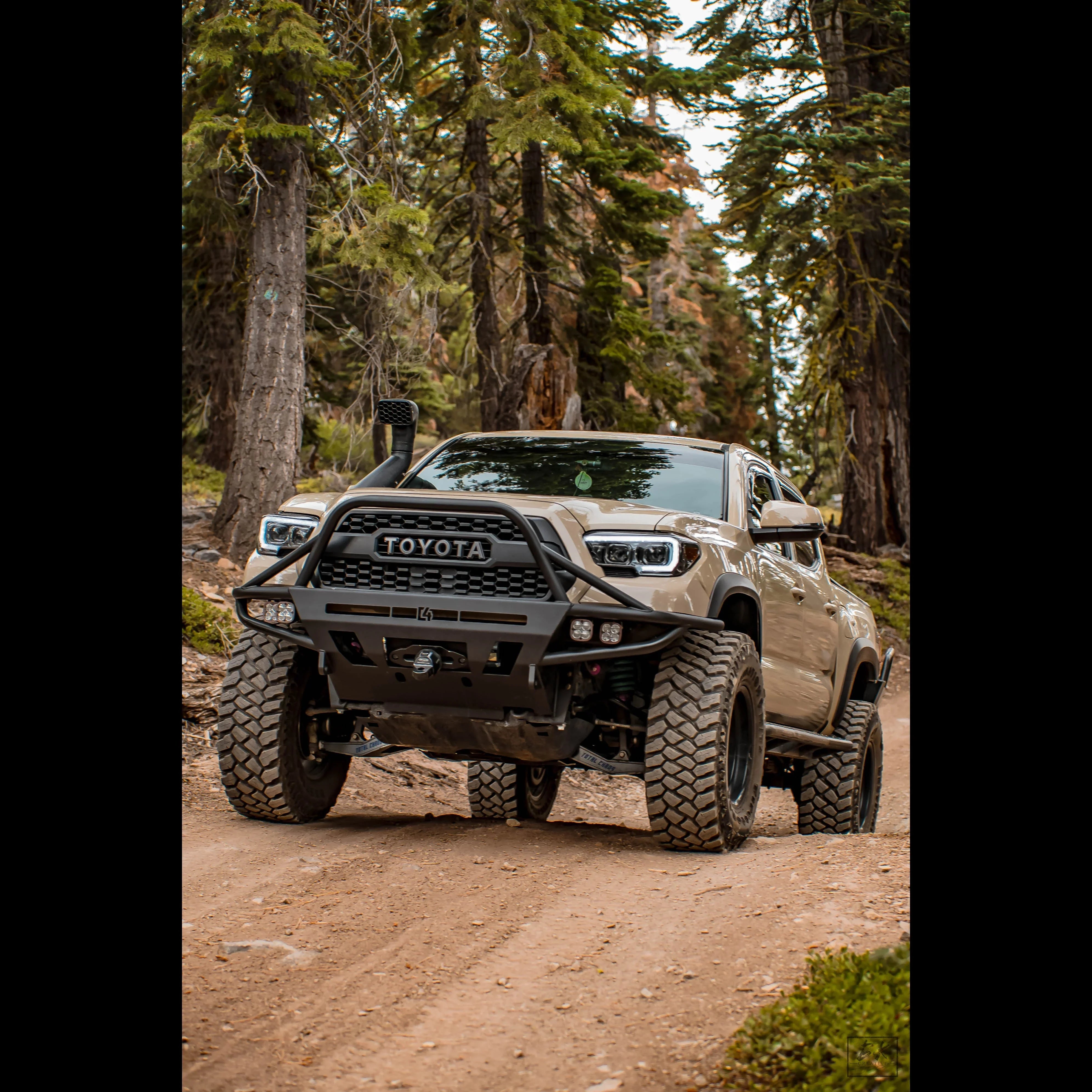 Lifted Toyota Tacoma with off-road accessories driving on a forest dirt trail