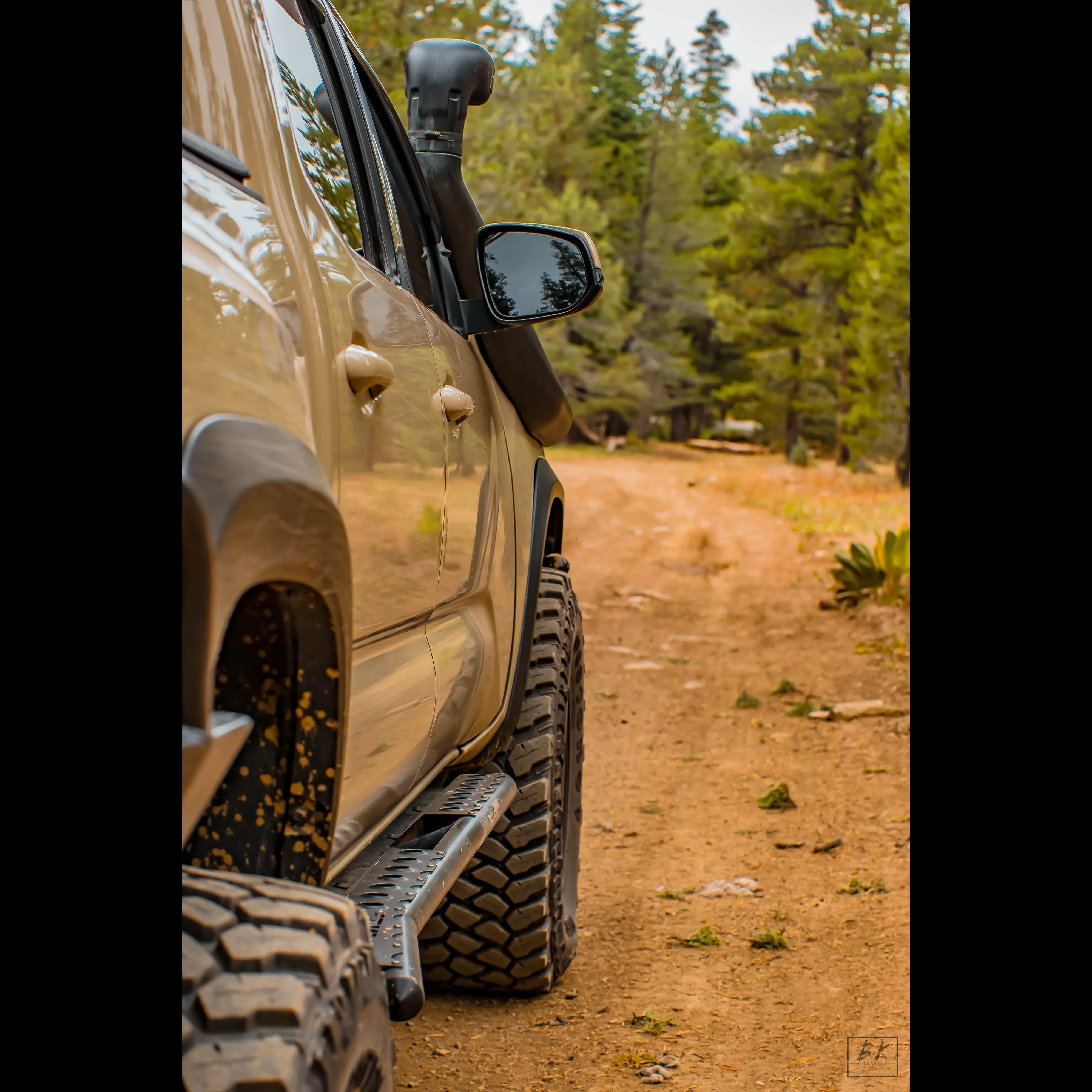 Off-road 4x4 vehicle with large all-terrain tires driving on a forest dirt trail