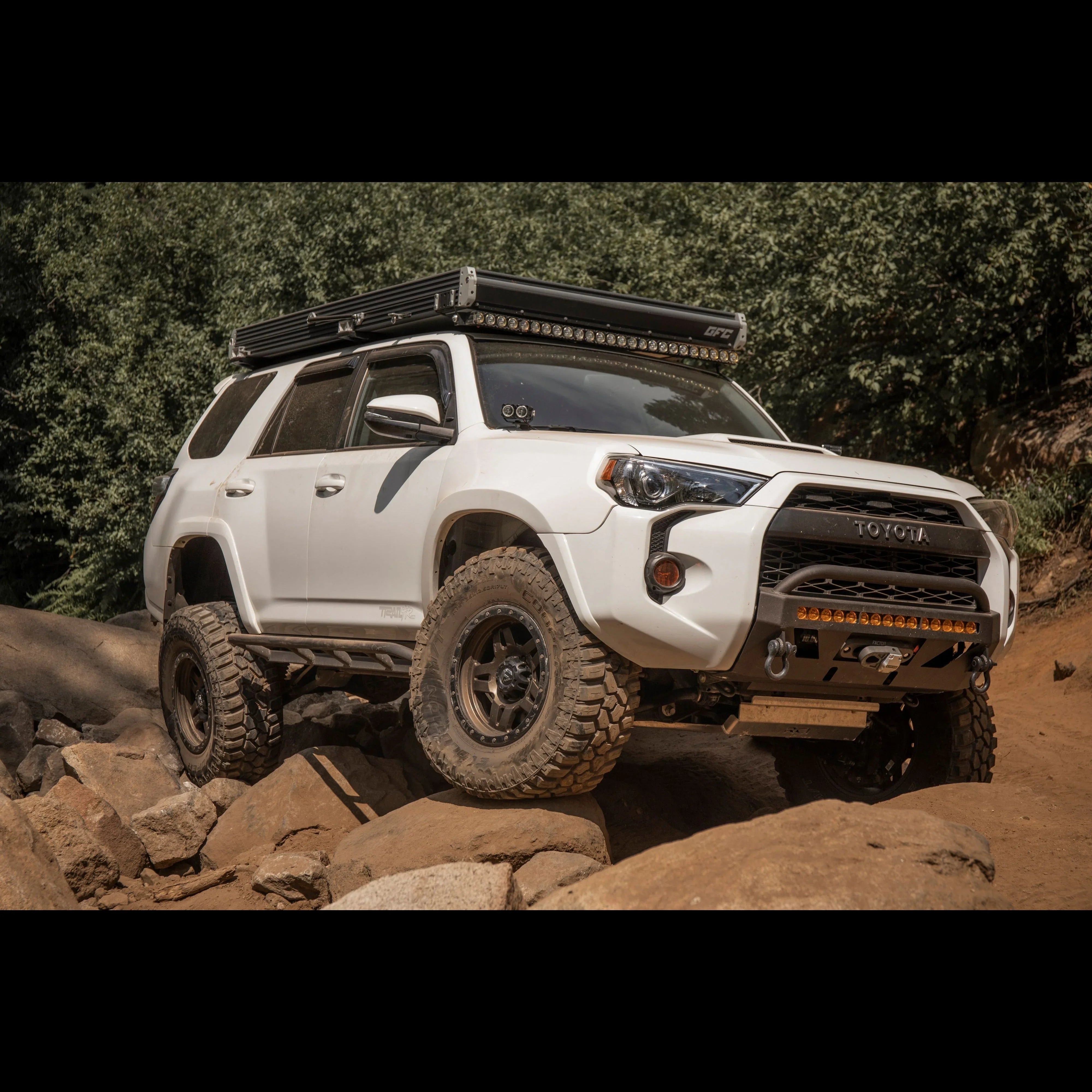 White Toyota 4Runner outfitted for overlanding with roof rack and off-road wheels on rocky trail