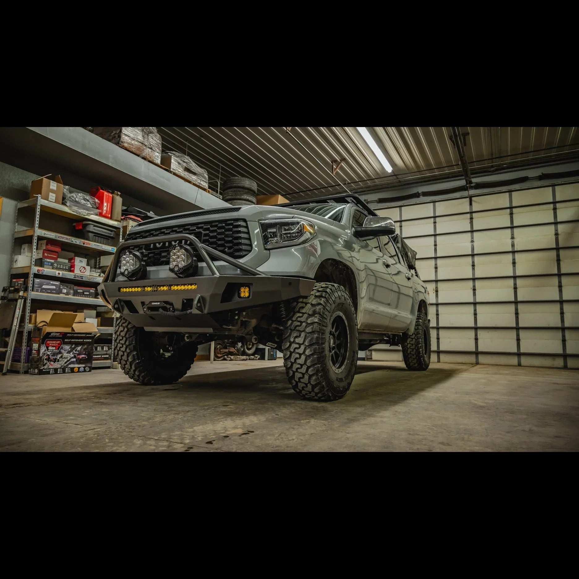 Lifted Toyota Tundra with off-road front bumper and lights in a garage setting