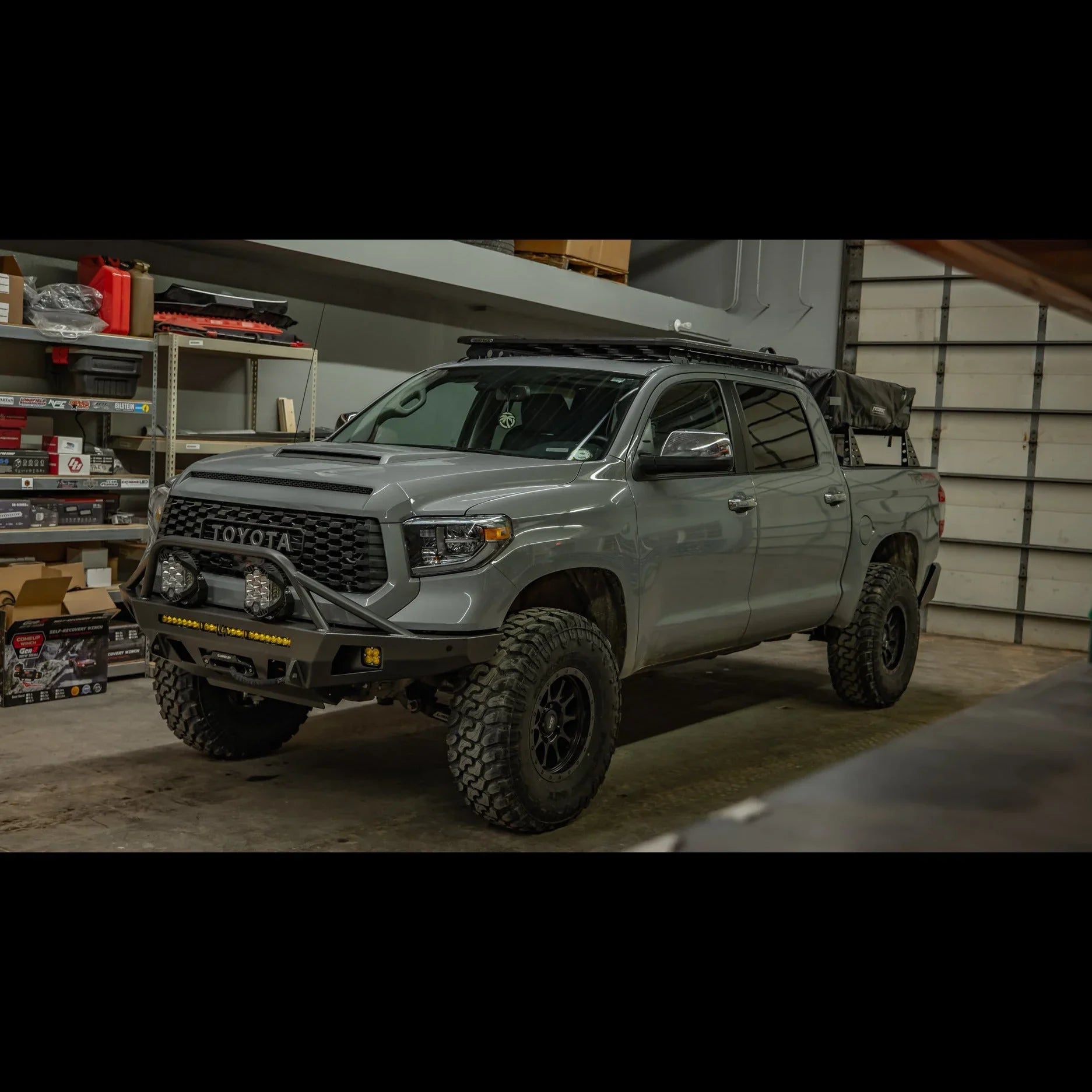 Toyota Tundra overland truck with off-road bumper and adventure gear in a garage