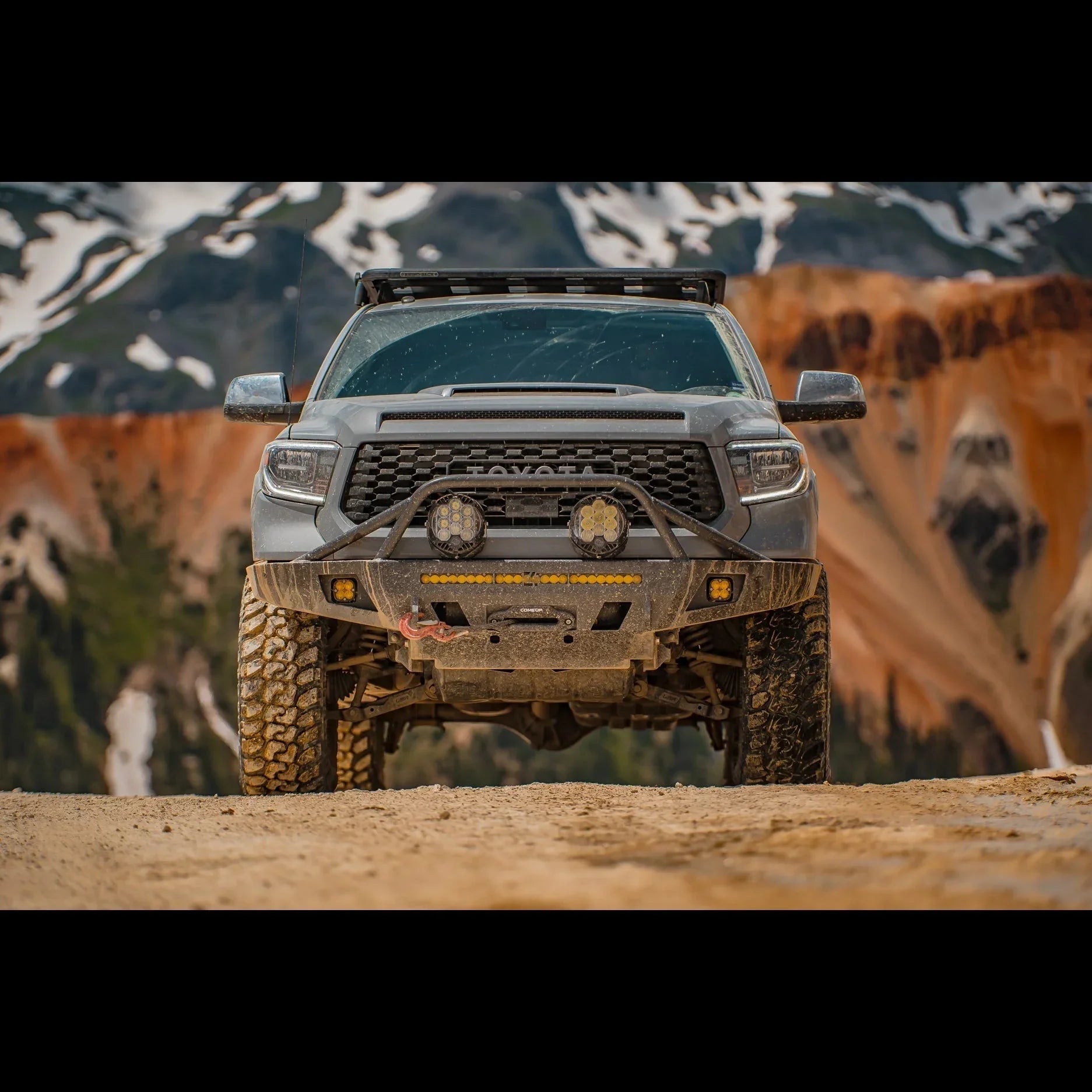 Toyota Tacoma with off-road bumper and lights on a dirt trail in a mountain landscape