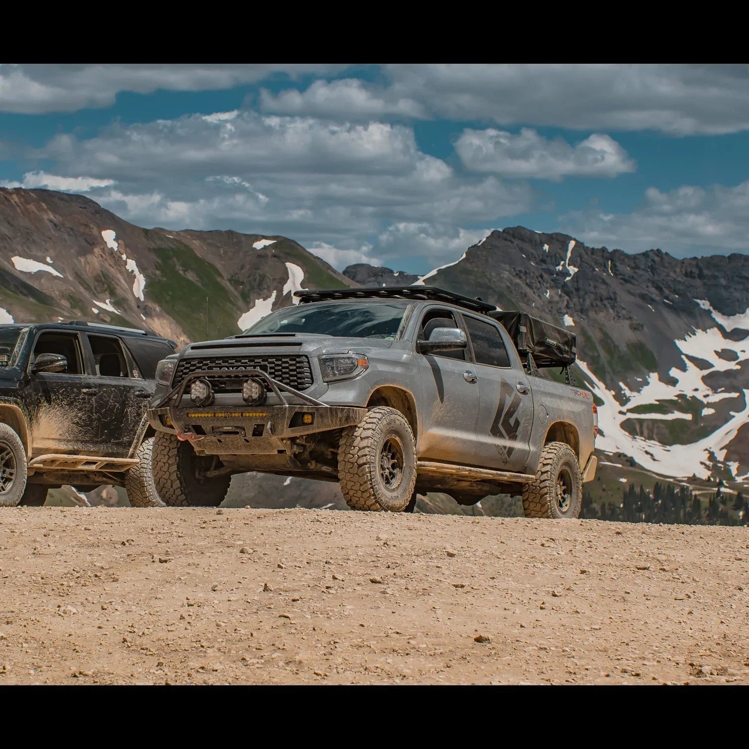 Lifted Toyota Tundra with off-road gear on a dirt mountain trail, rugged terrain, adventure vehicle.