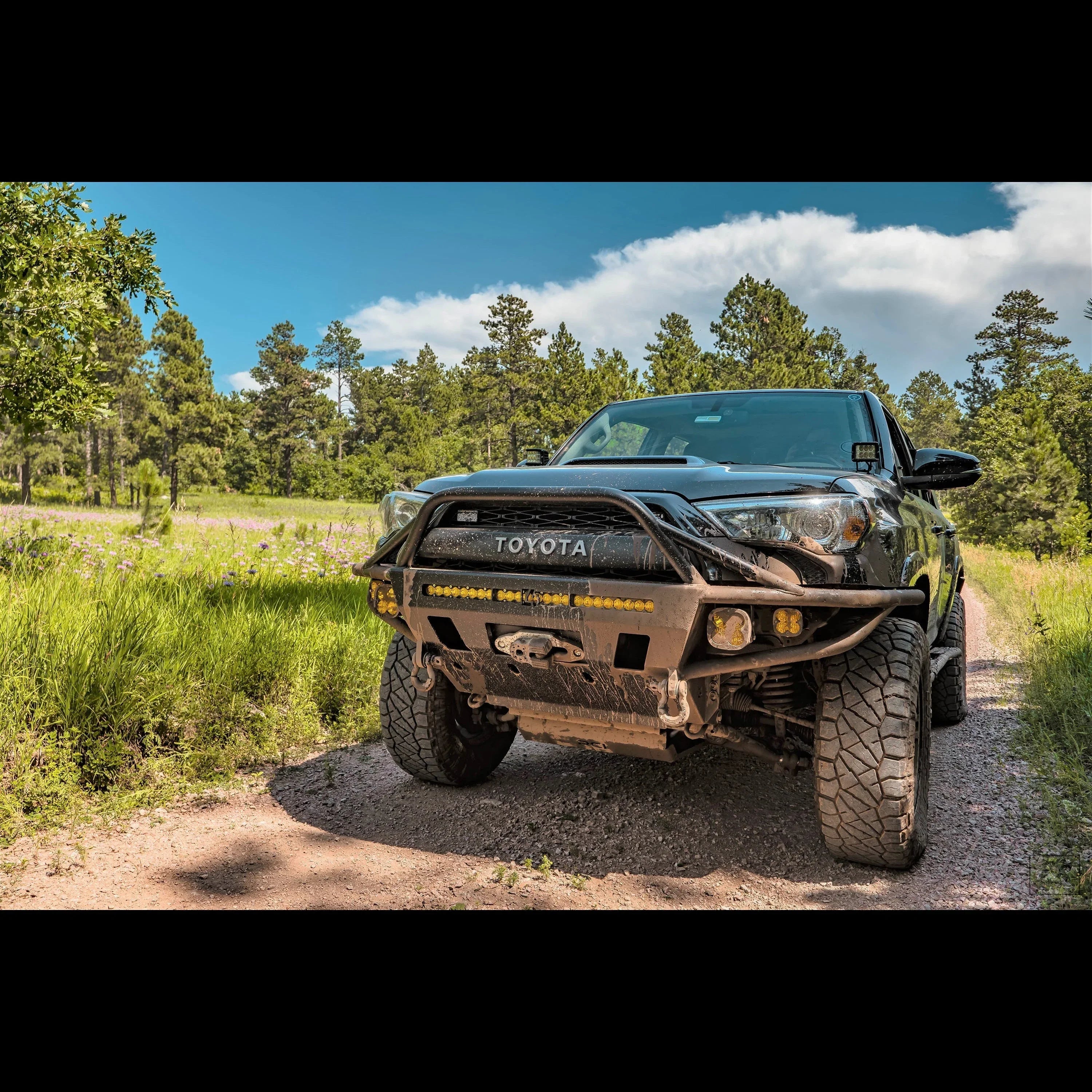 Toyota Tacoma off-road truck with rugged front bumper and mud tires on a forest trail