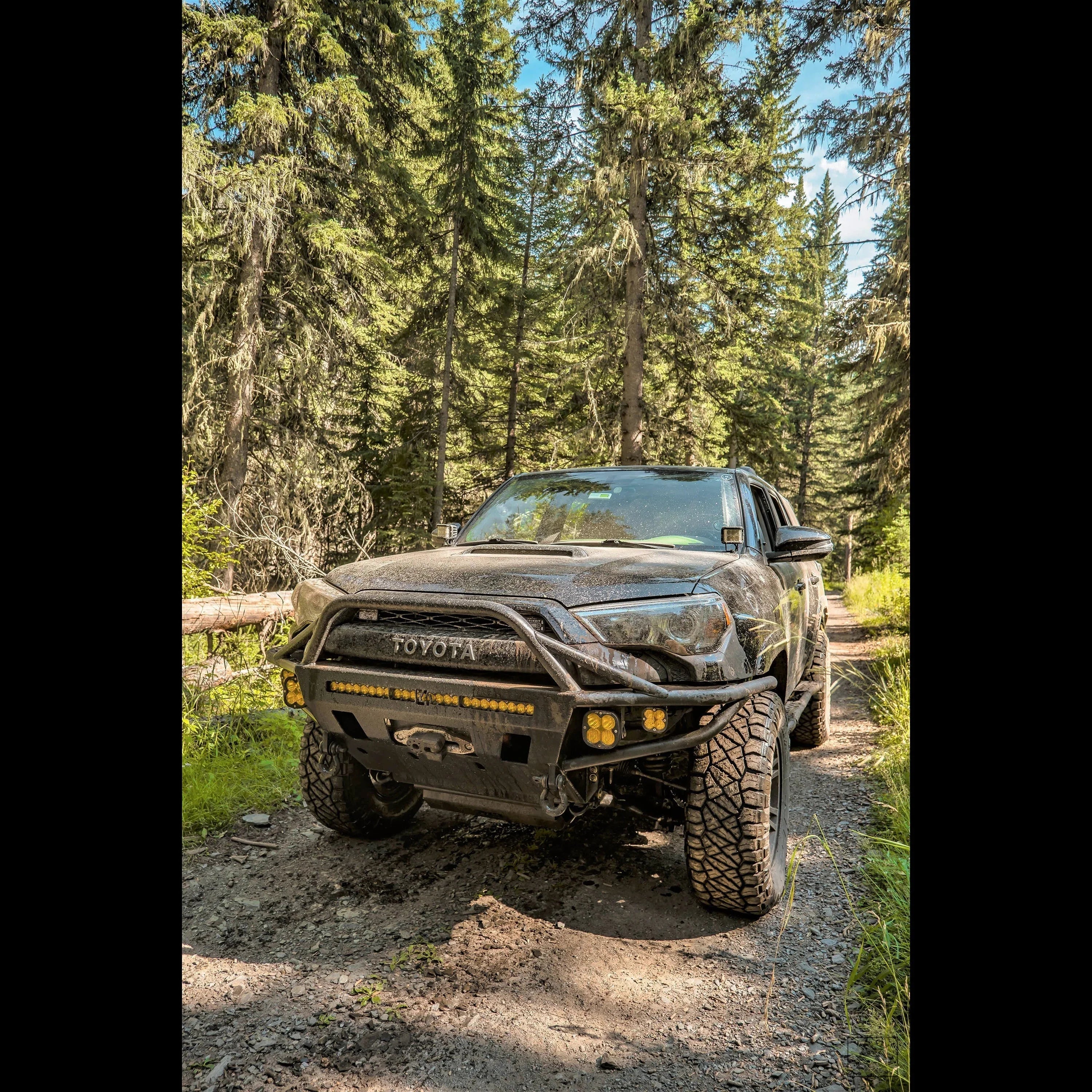 Toyota Tacoma with off-road bumper and mud tires on forest trail for overlanding adventure