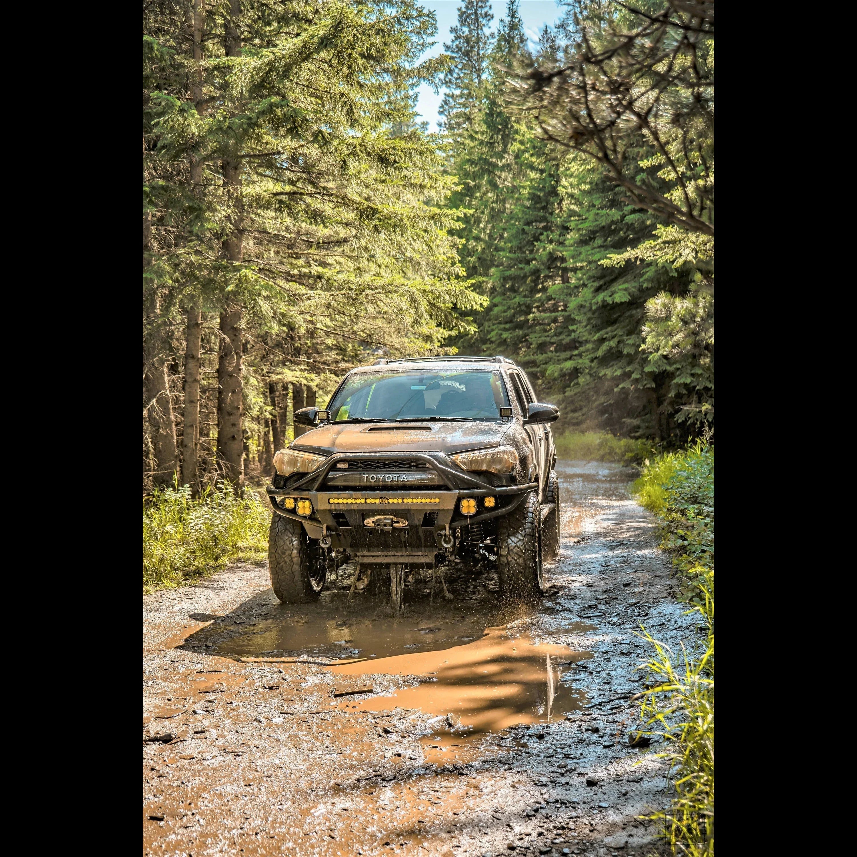 Toyota 4Runner off-road vehicle driving through muddy forest trail, overlanding gear visible