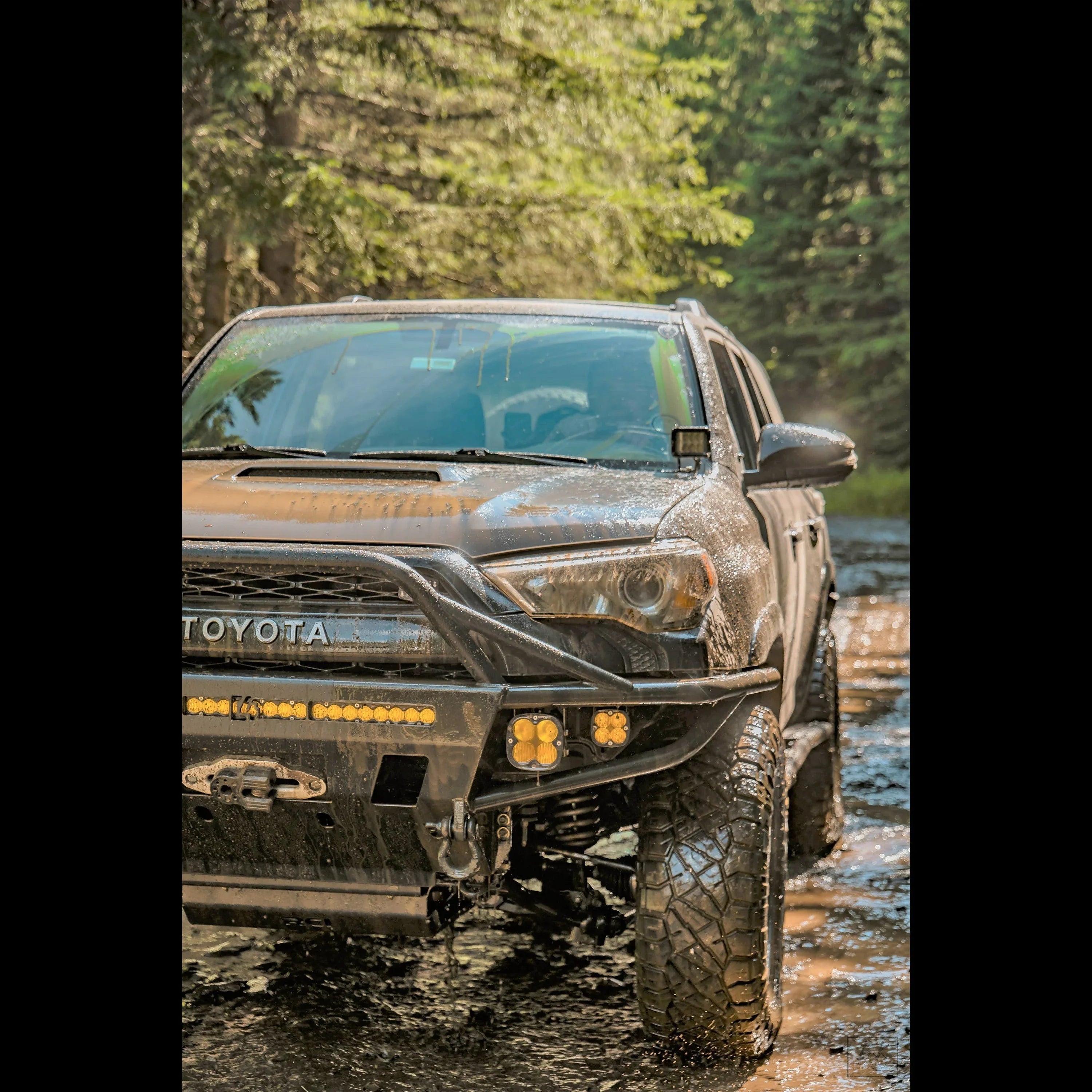 Toyota 4Runner with off-road bumper and LED lights crossing a muddy forest trail