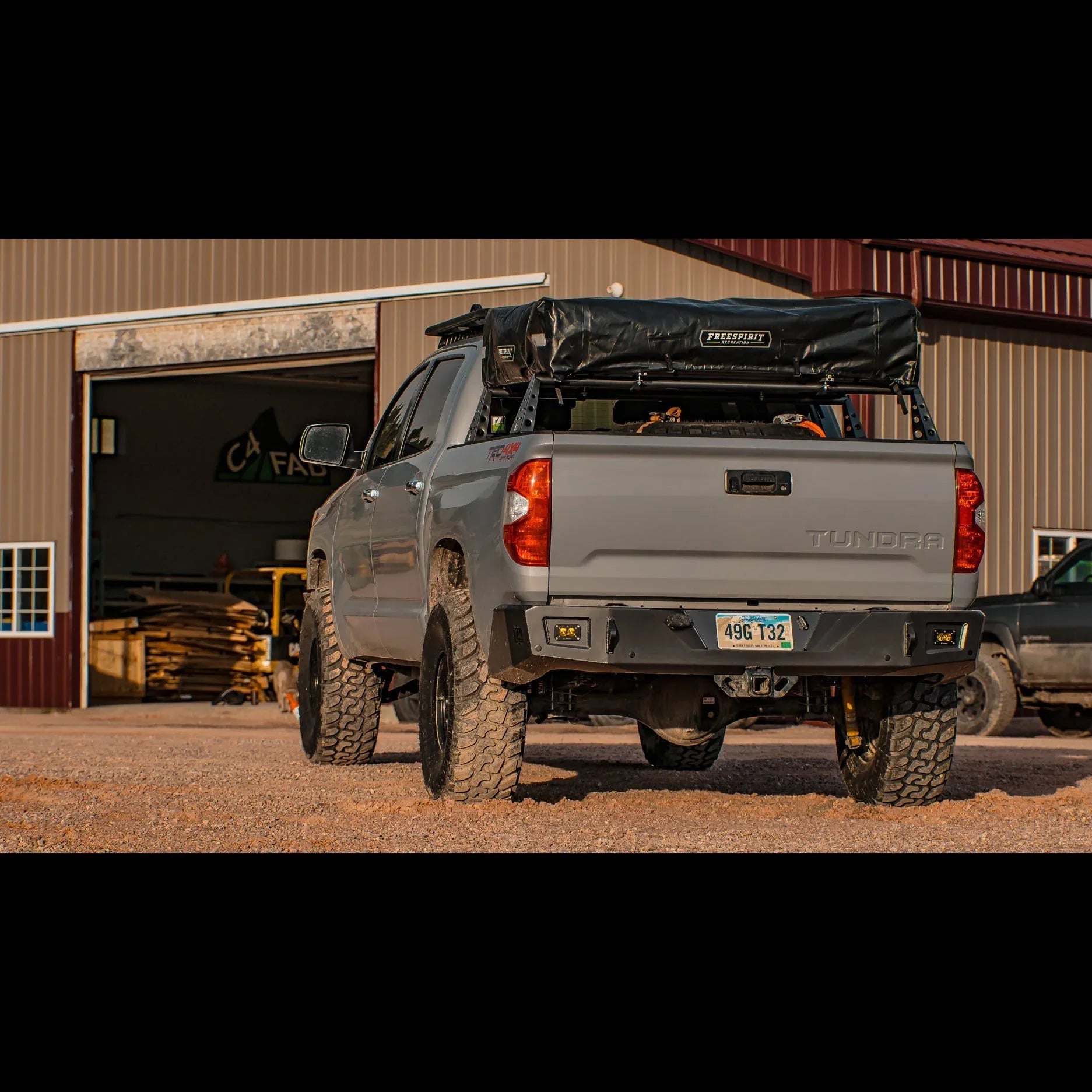 Toyota Tundra with off-road rear bumper and rooftop tent parked outside metal workshop