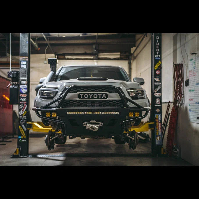 Lifted Toyota Tacoma with off-road bumper, snorkel, and LED lights in a garage