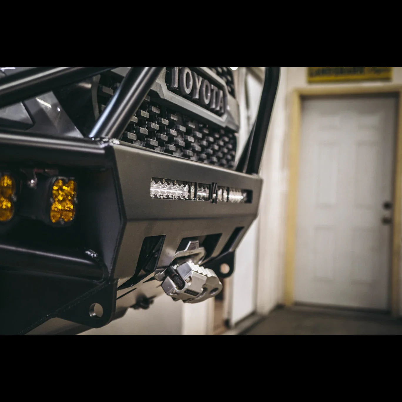 Toyota Tacoma aftermarket front bumper with LED lights and winch in garage setting
