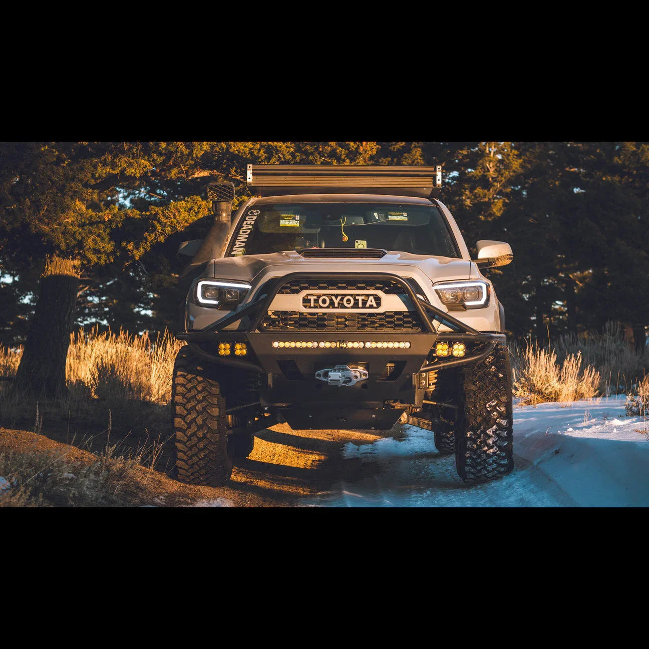 Toyota Tacoma with off-road bumper, LED lights, and tire upgrade parked on snowy trail