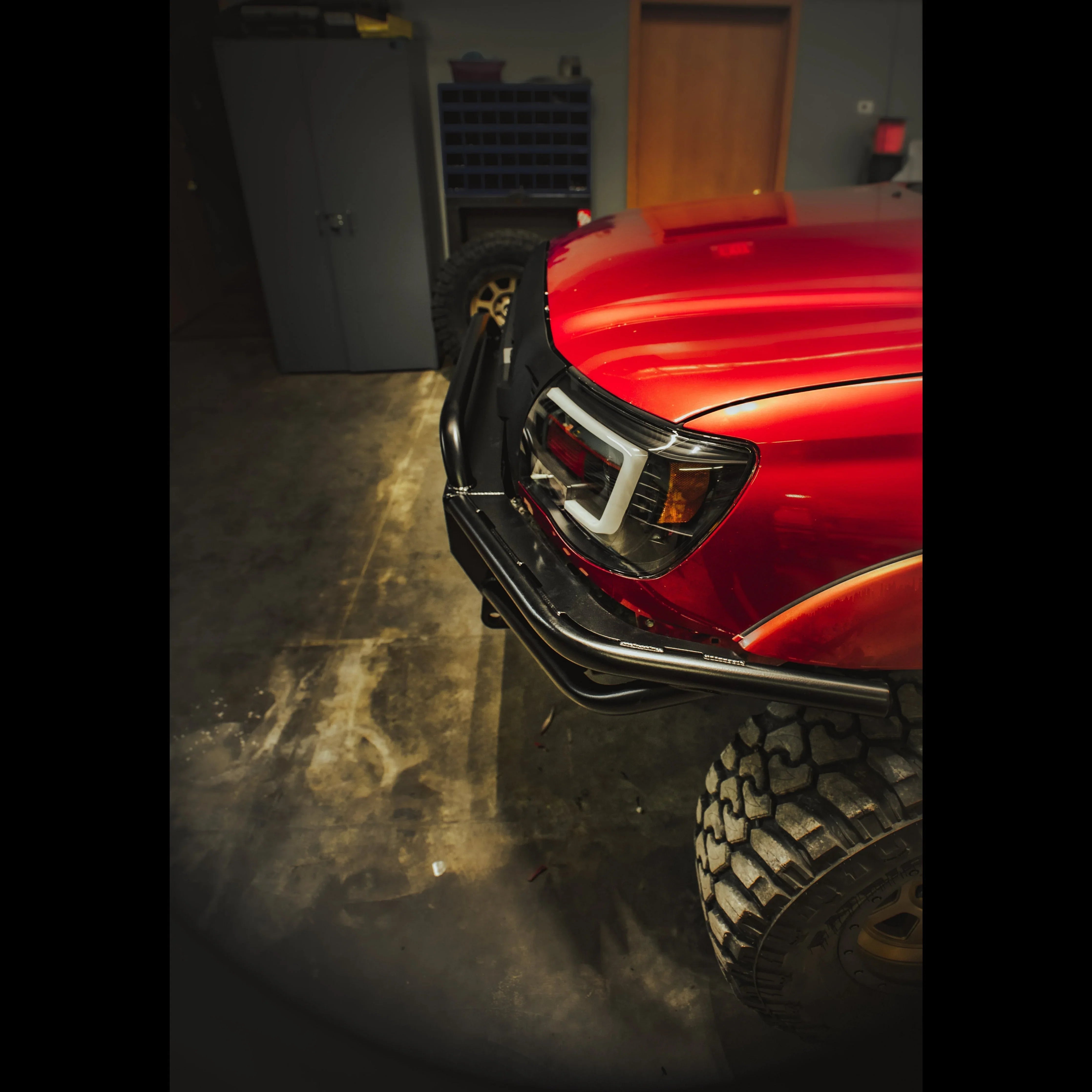Red Toyota Tacoma with off-road steel bumper and rugged all-terrain tires in garage