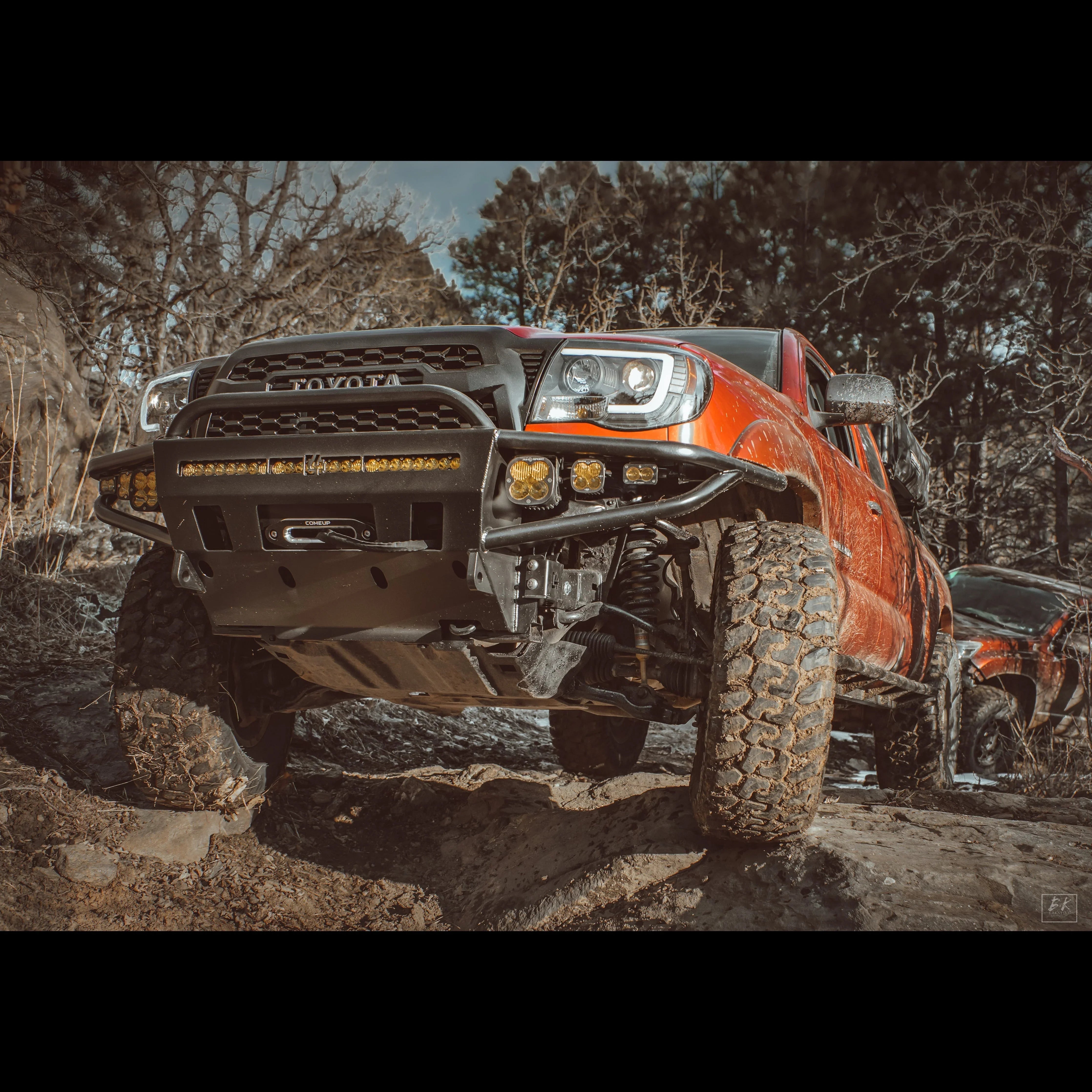 Lifted Toyota Tacoma off-road truck with aftermarket bumper and lights on rocky trail