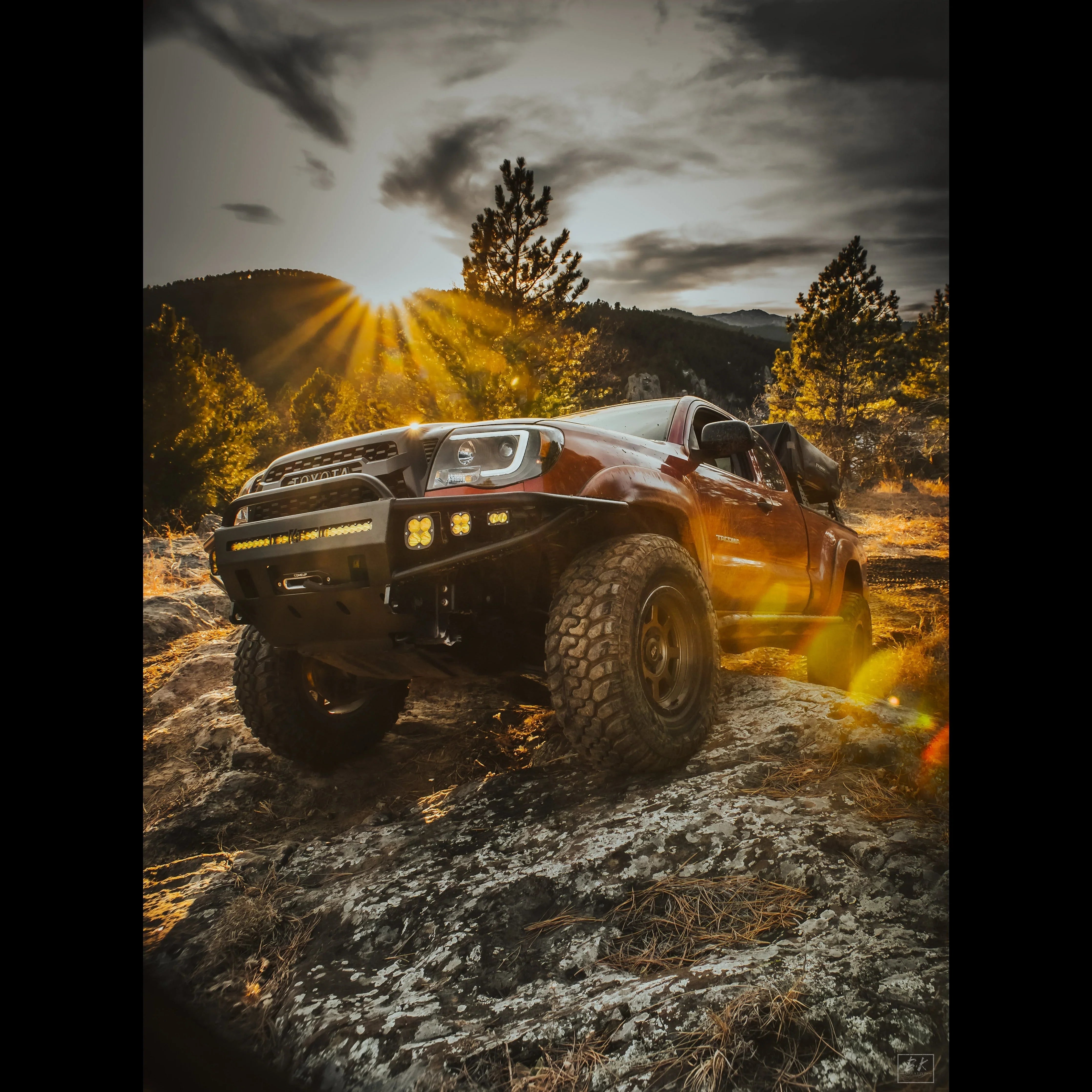 Lifted Toyota Tacoma with off-road accessories and LED lights on a rocky mountain trail at sunset