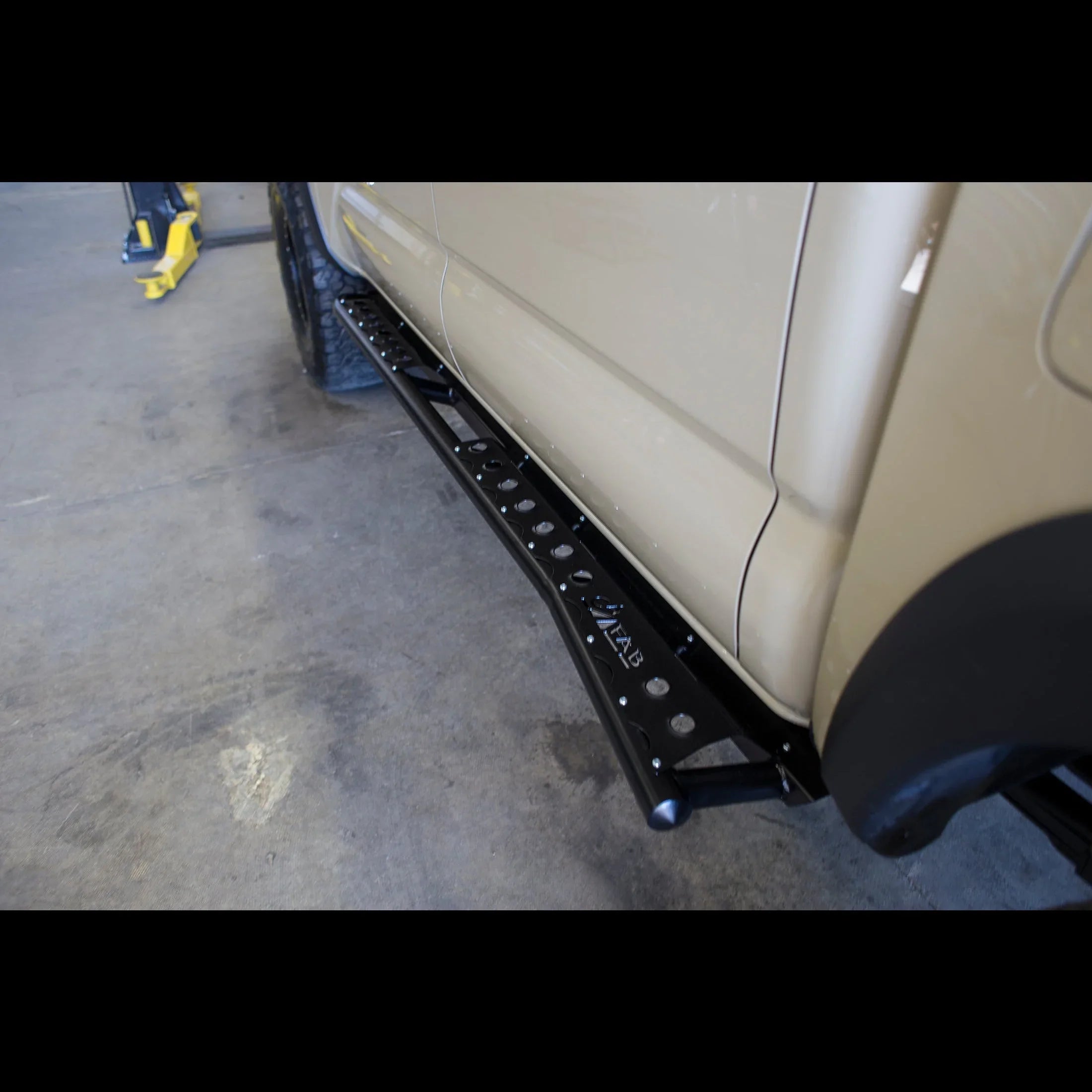 Black off-road rock slider step installed on beige Toyota truck for overlanding protection