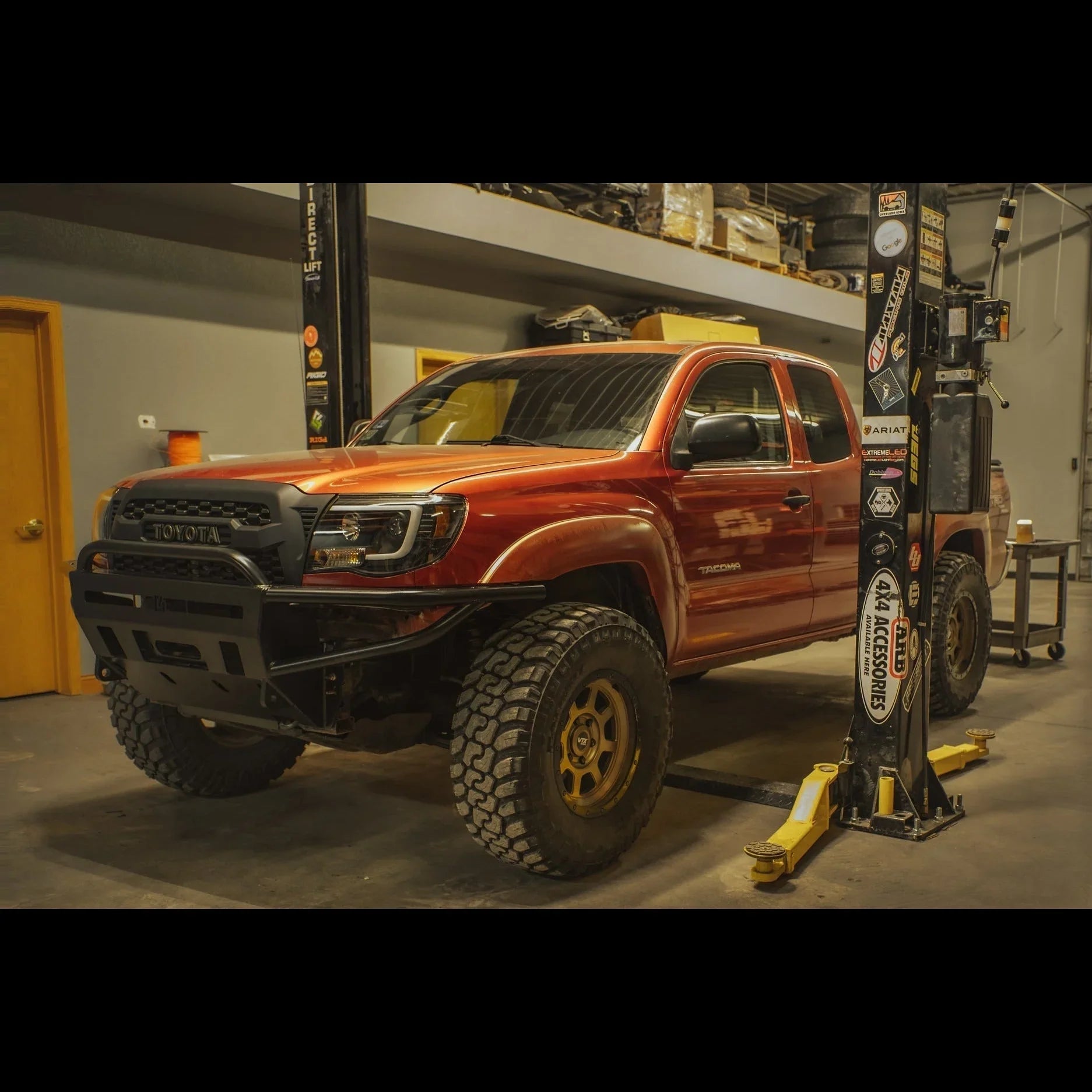 Lifted Toyota Tacoma with off-road tires and custom front bumper in a garage workshop