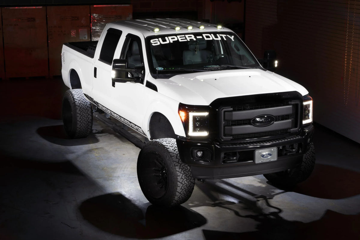 Lifted white Ford Super Duty truck with LED lights and off-road tires in a garage setting