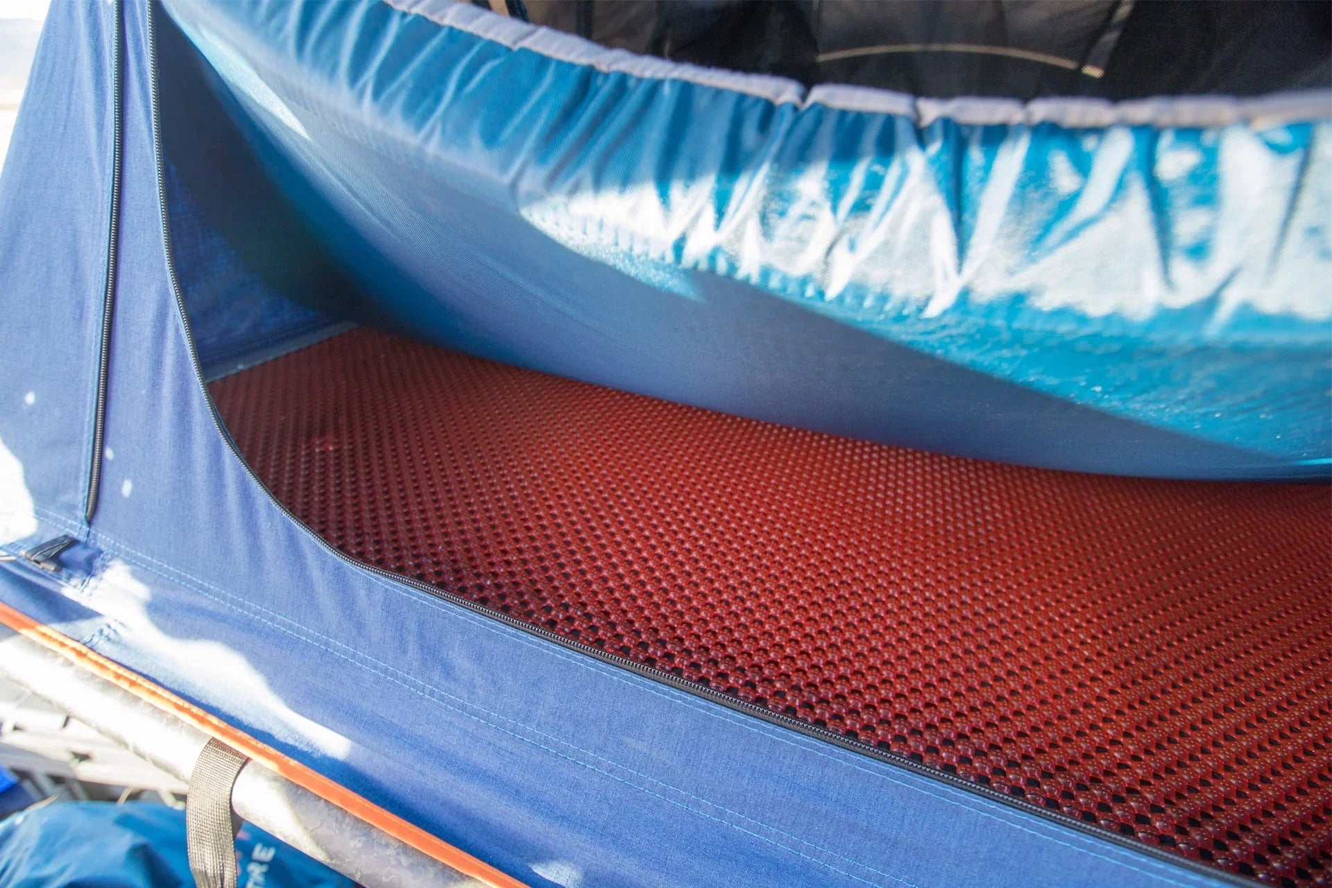 Red honeycomb anti-condensation mat inside blue rooftop tent for overlanding vehicles