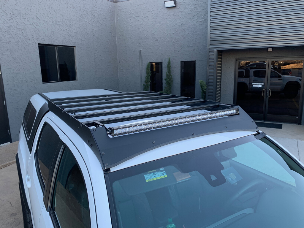 Toyota Tacoma with overland roof rack and LED light bar in modern building setting