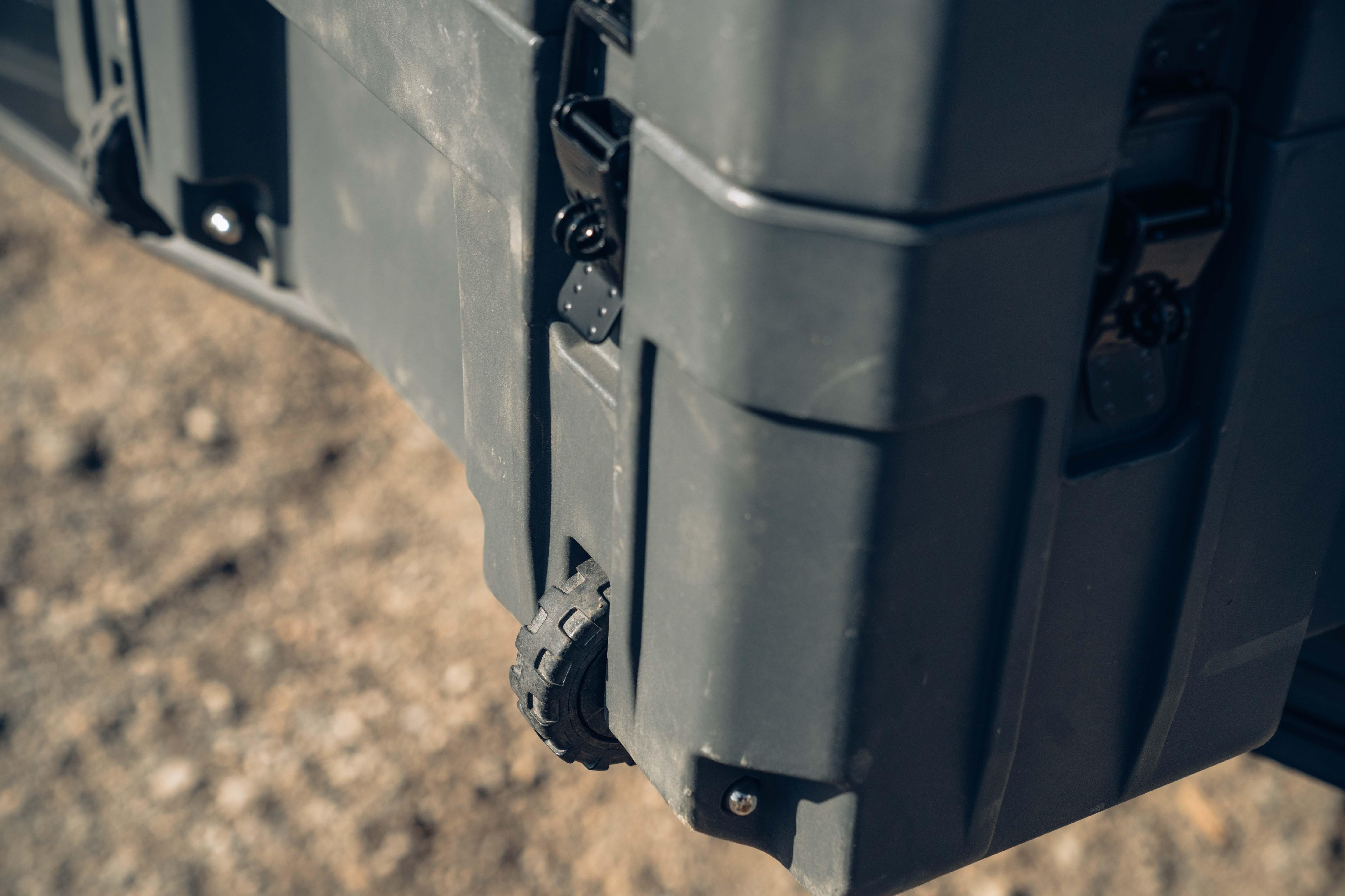 Heavy-duty black storage case with rugged wheel for overlanding, on outdoor terrain