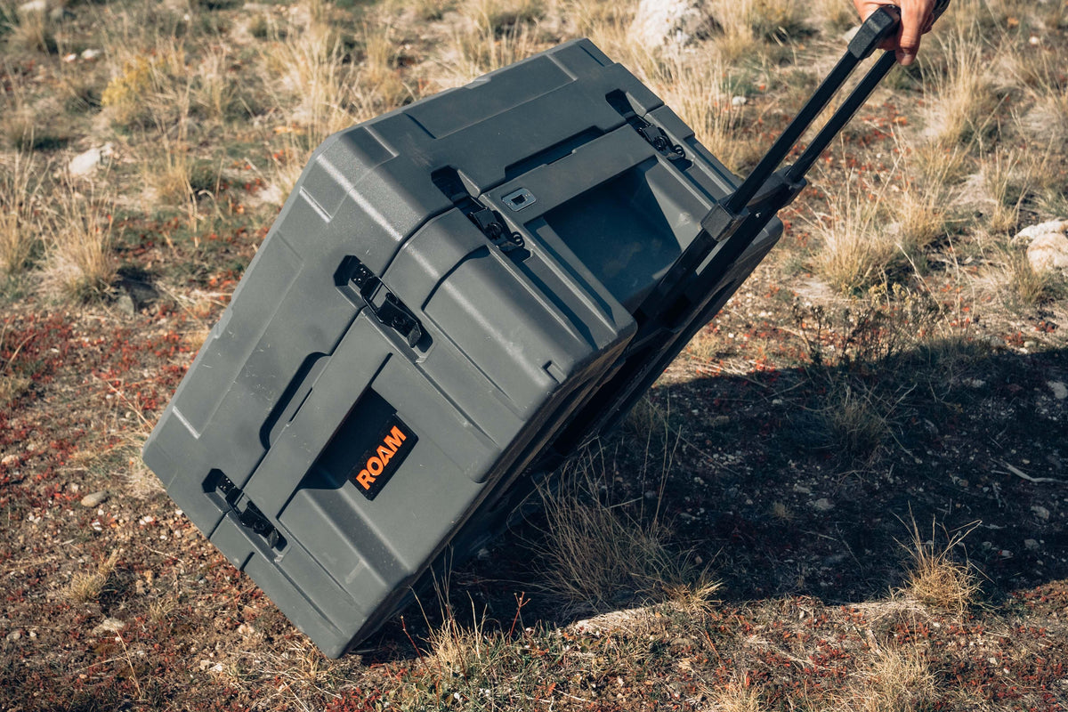Rugged wheeled storage case for overlanding, shown on rocky outdoor terrain