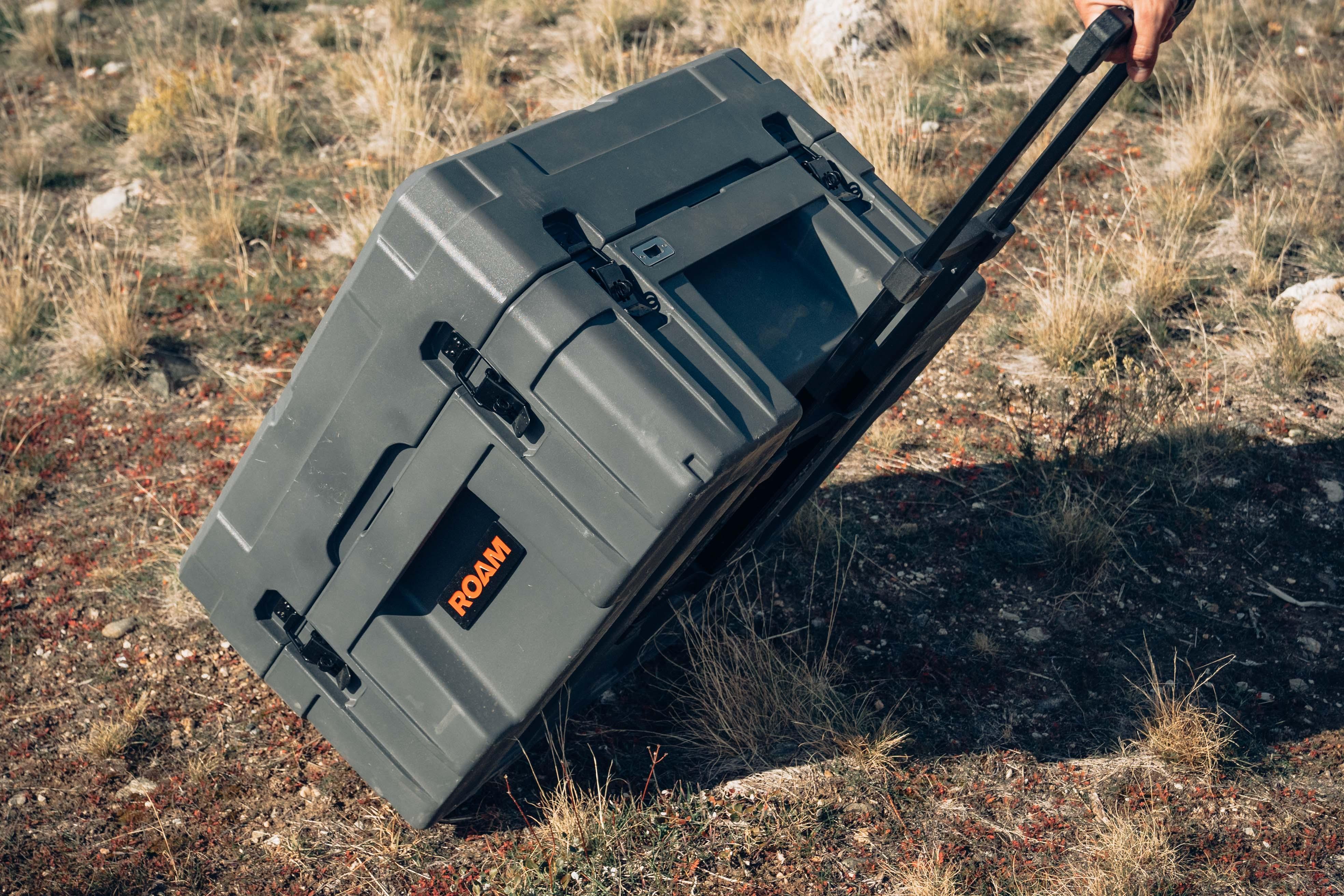 Rugged wheeled storage case for overlanding, shown on rocky outdoor terrain