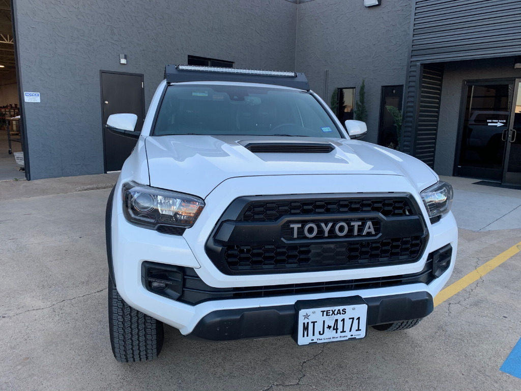White Toyota Tacoma with aftermarket grille and LED light bar parked outside a building