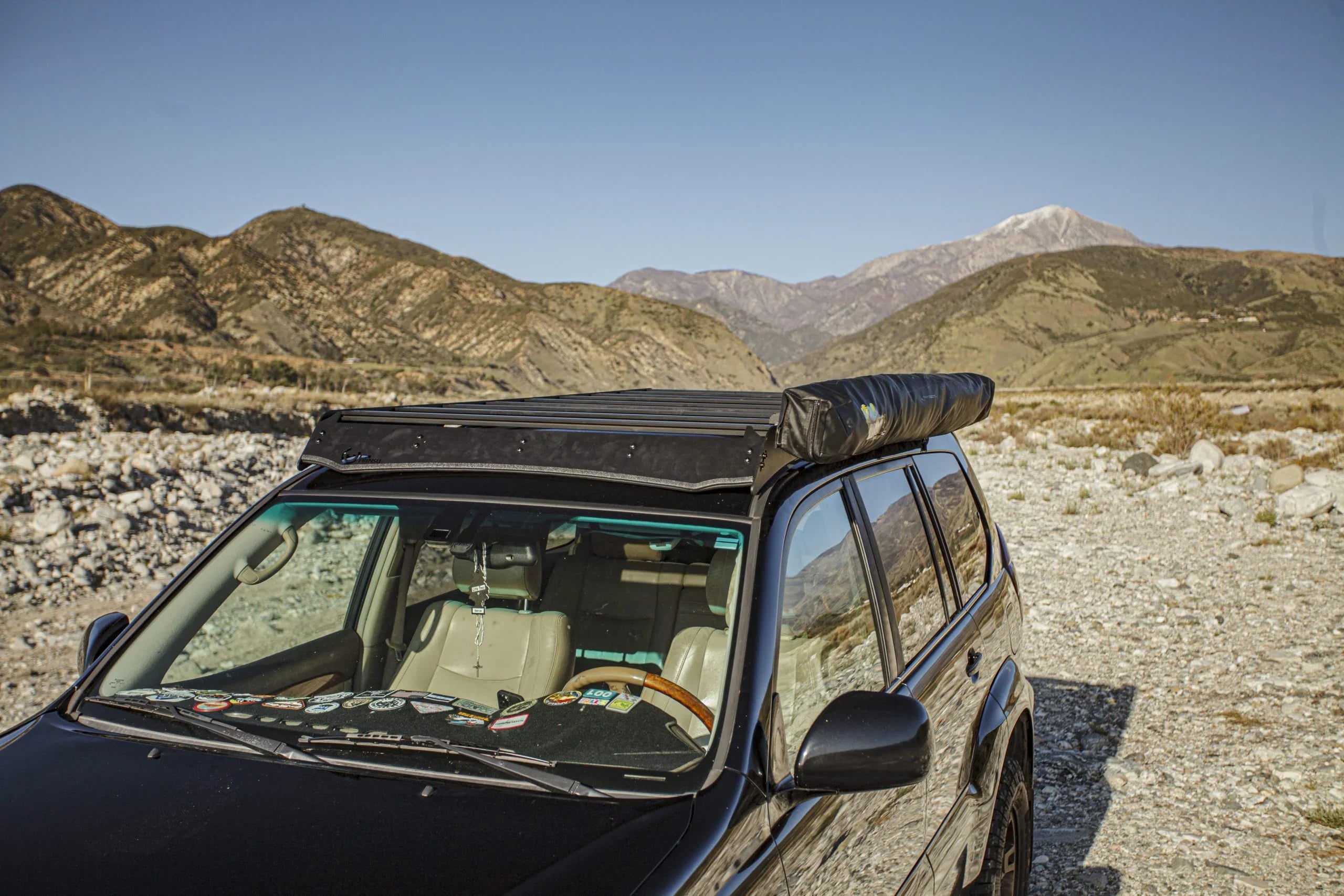 SUV with roof rack and awning parked off-road in rocky mountain landscape