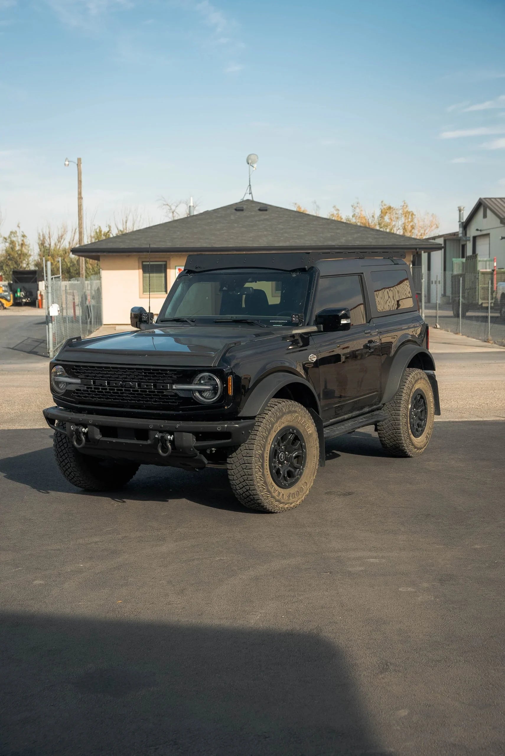 Black 2-door Ford Bronco with off-road roof rack and all-terrain tires in outdoor setting