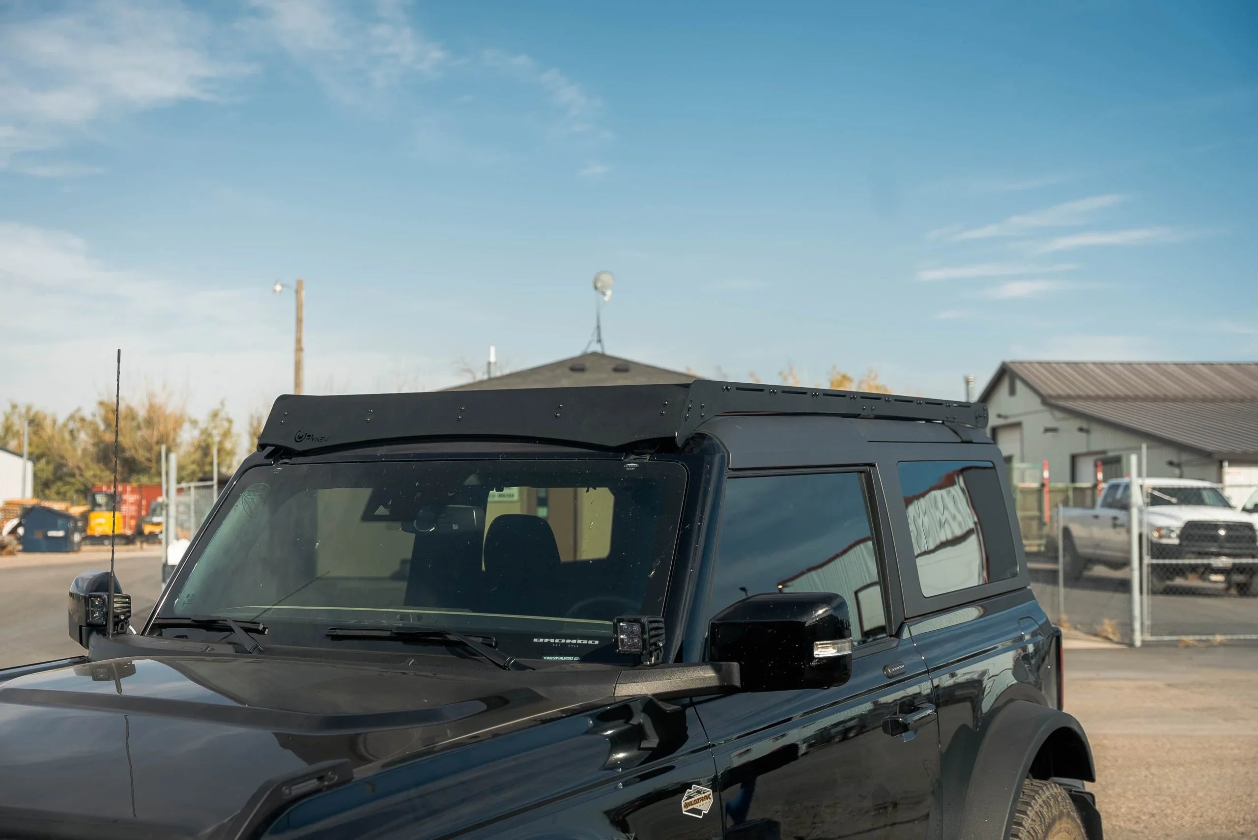 Black Ford Bronco 2-door with roof rack in outdoor lot, overlanding vehicle accessories visible