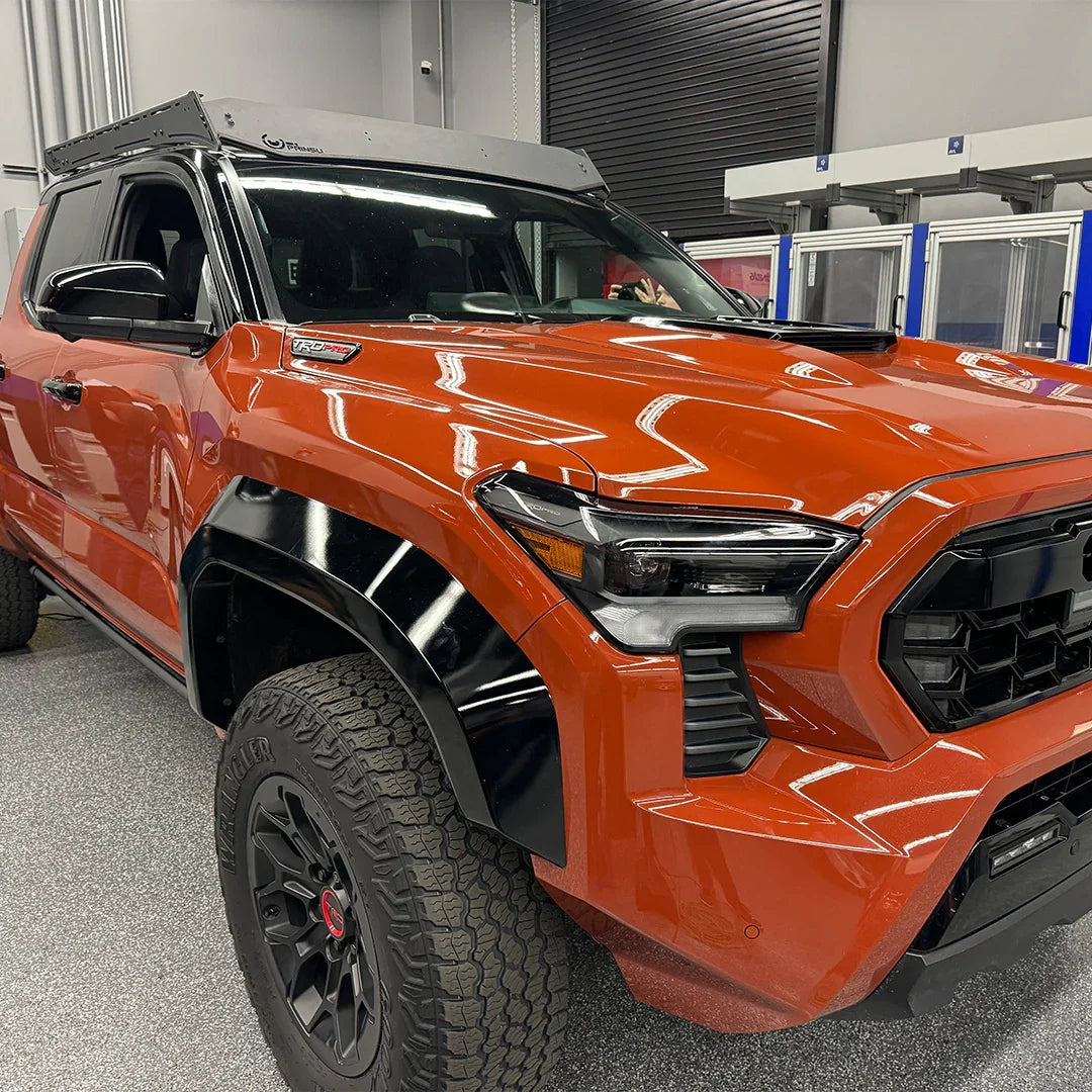 2024 Toyota Tacoma TRD Pro in orange with black fender flares and roof rack in a garage