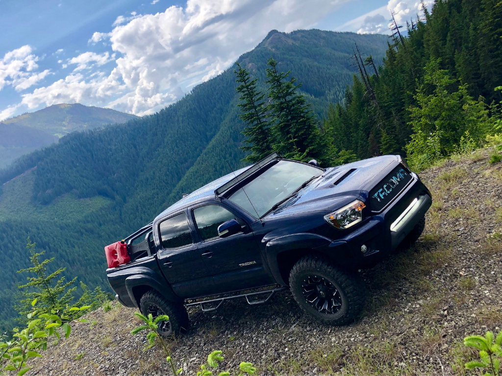 Black Toyota Tacoma overland truck with off-road accessories on a mountain trail