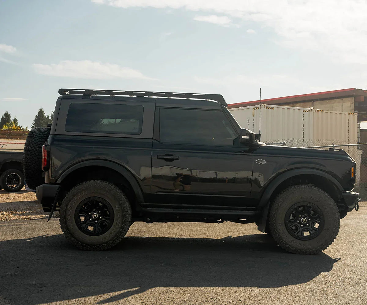 Black 2-door Ford Bronco with roof rack, off-road tires, parked outdoors