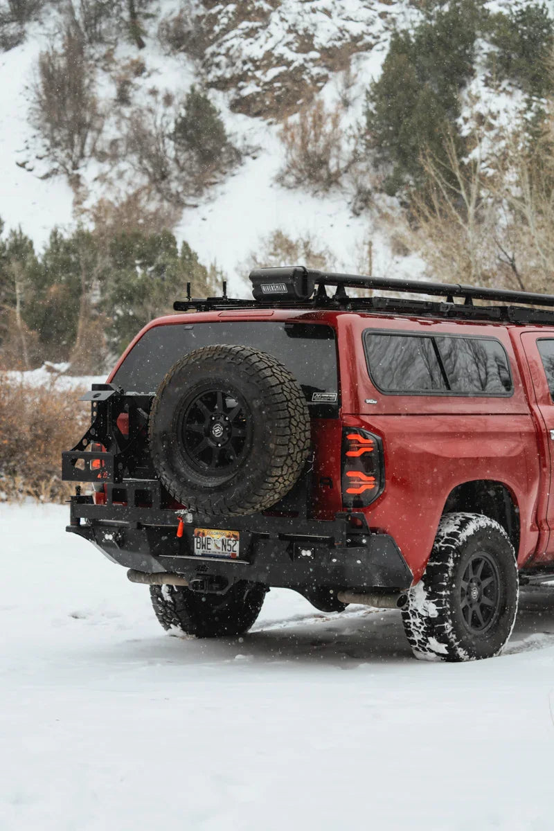 Toyota Tundra with rear swing arm bumper, spare tire, and roof rack in snowy landscape