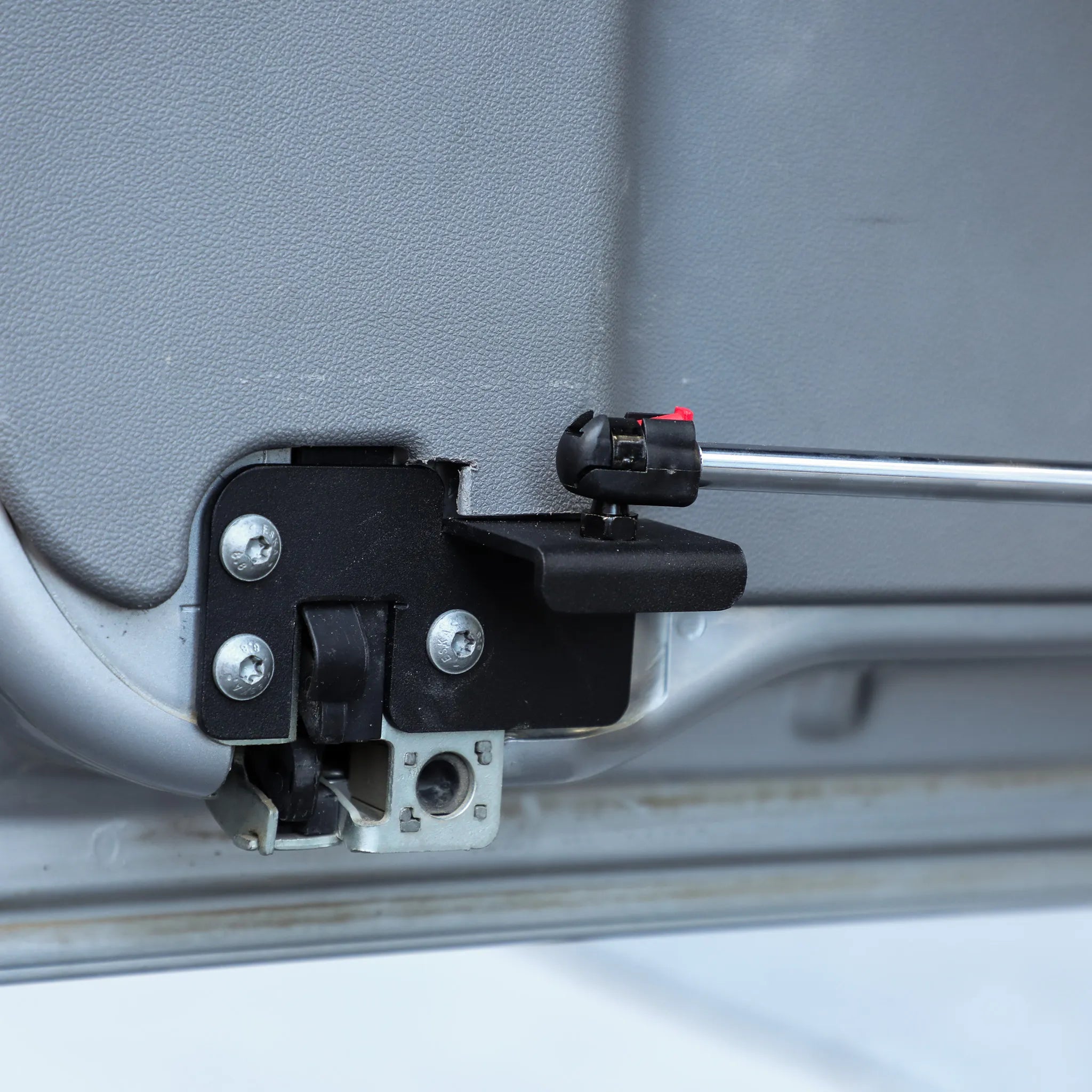 Close-up of a vehicle rear hatch lock mechanism with metal strut for overland accessory installation.