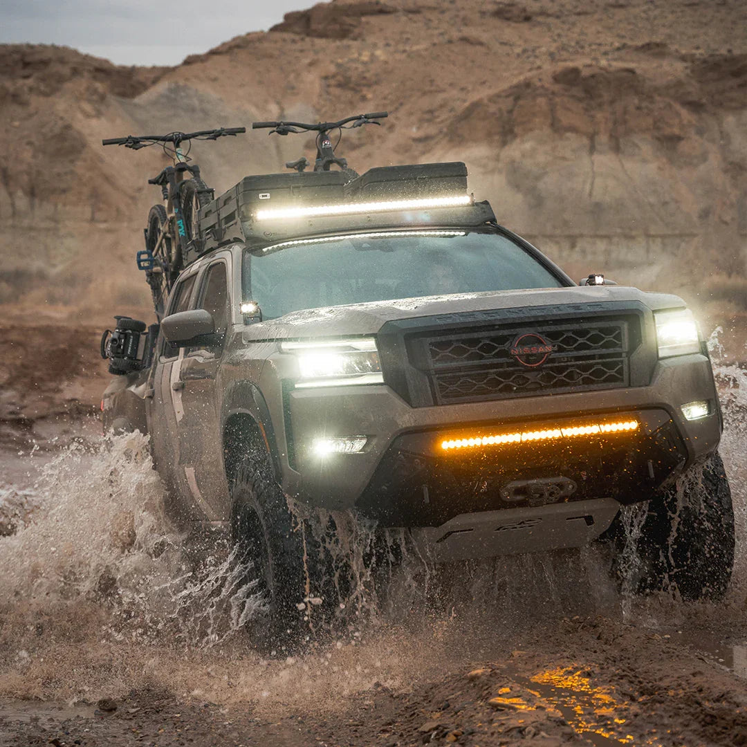 3rd gen Nissan Frontier with off-road skid plates and gear tackling rugged muddy terrain