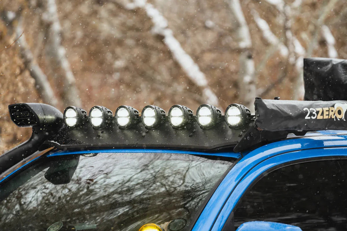 Toyota Tacoma with roof-mounted LED off-road lights and gear in snowy outdoor setting