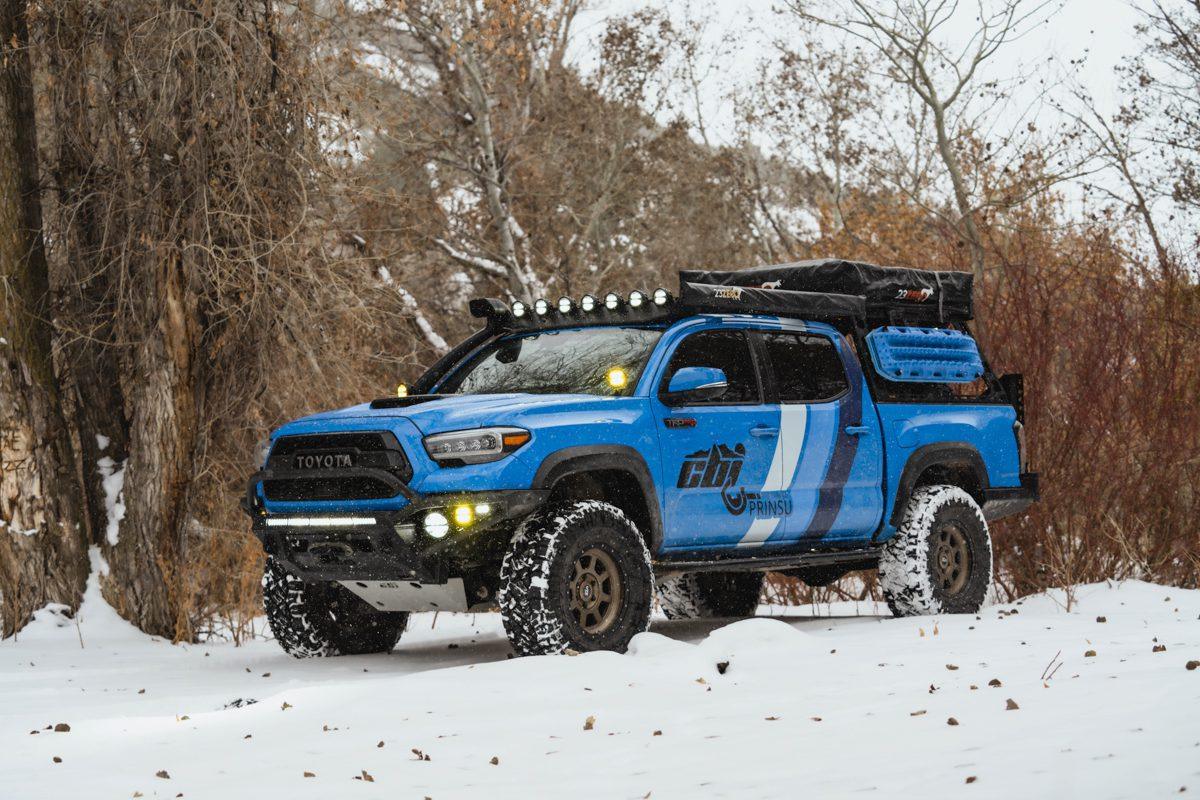 Blue Toyota Tacoma with off-road overlanding accessories parked in snowy forest