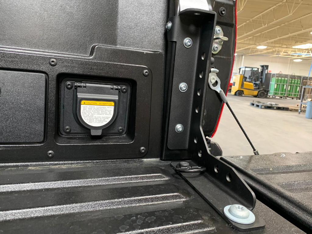 Truck bed tailgate with heavy-duty steel mounting bracket and power outlet, warehouse background