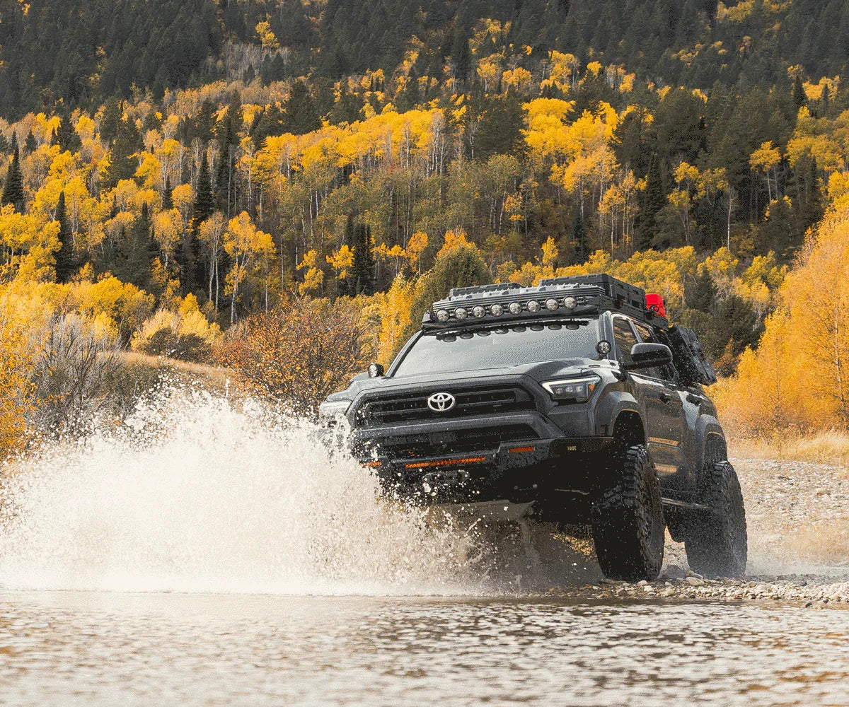 Toyota 4Runner outfitted for overlanding driving through water with fall forest in background