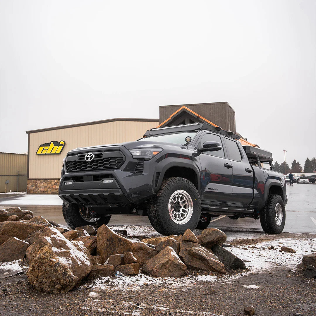 4th gen Toyota Tacoma with off-road armor and rooftop tent parked on snowy rocks