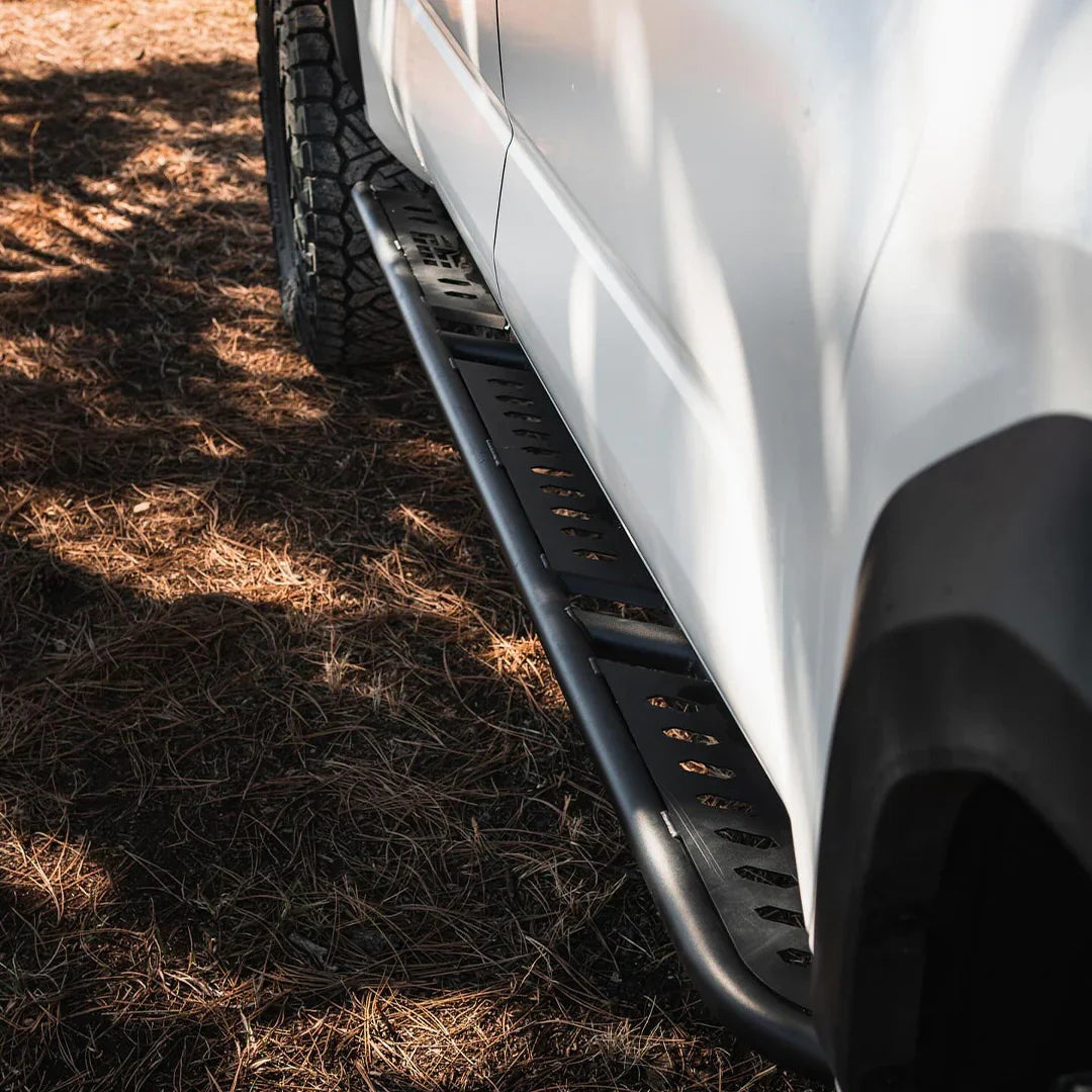 Black rock sliders installed on a white Toyota Tacoma truck, side view outdoors