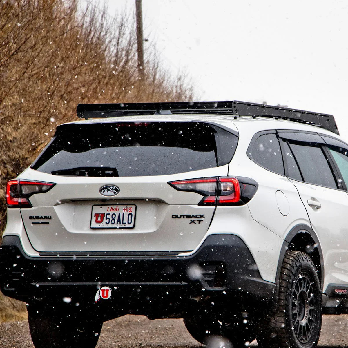 White Subaru Outback XT with roof rack and off-road tires in snowy outdoor setting